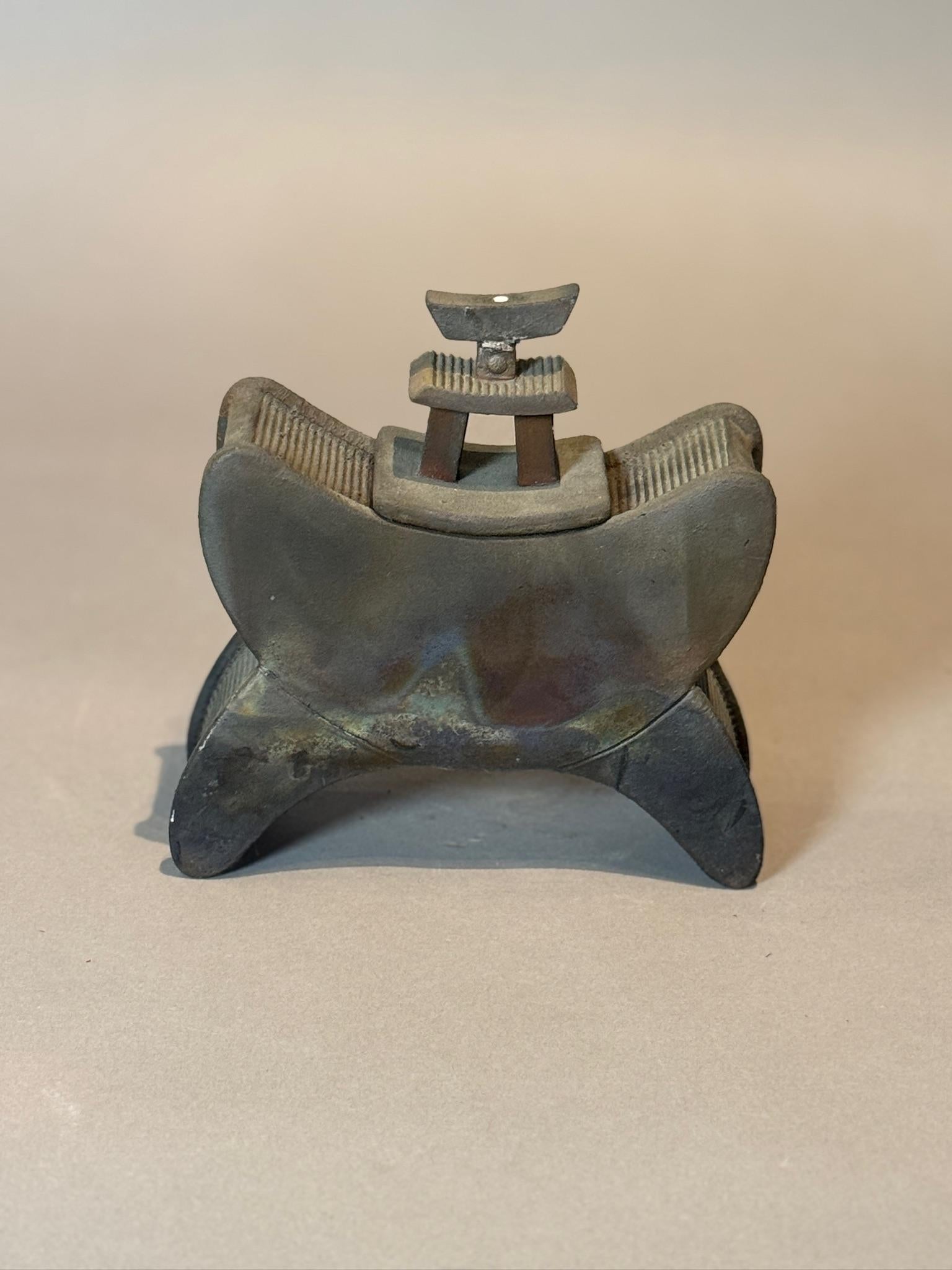 Esta llamativa escultura de cerámica moderna está inspirada en los reposacabezas y objetos rituales tradicionales de Asia. Elaborada con una forma escultural y curvada y con intrincados detalles estriados, esta pieza emana una sensación tanto de
