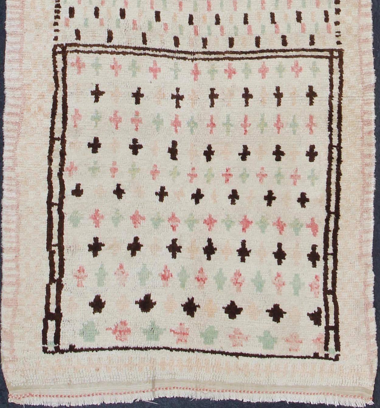 Unique Moroccan Runner in Light Ivory Background & Brown, Rose, Green Accents.
Featuring cross shapes in an assortment of neutral colors, this unique Moroccan has an abstract flair. With three central flower motifs, it is an artistic and original