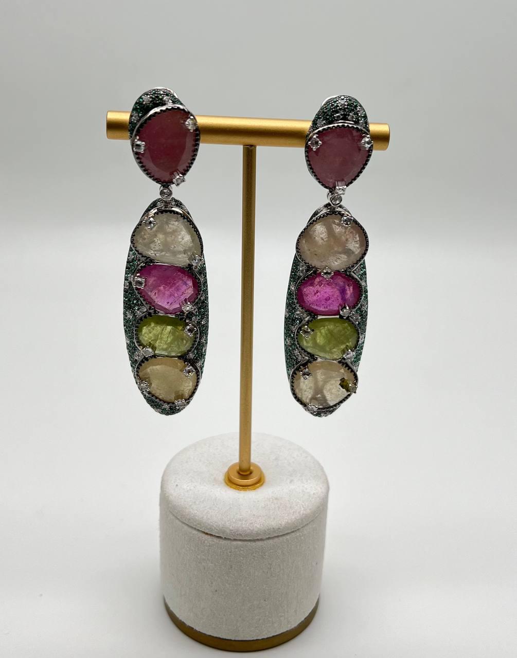 Ohrringe mit mehrfarbigen Saphiren, die in einer vertikalen Anordnung von 57,23 Karat gefasst sind. Der oberste Stein ist ein tiefes Rosa, gefolgt von einer Reihe durchscheinender und leuchtender Steine in Rosa-, Grün- und Klar-Tönen. Die Steine
