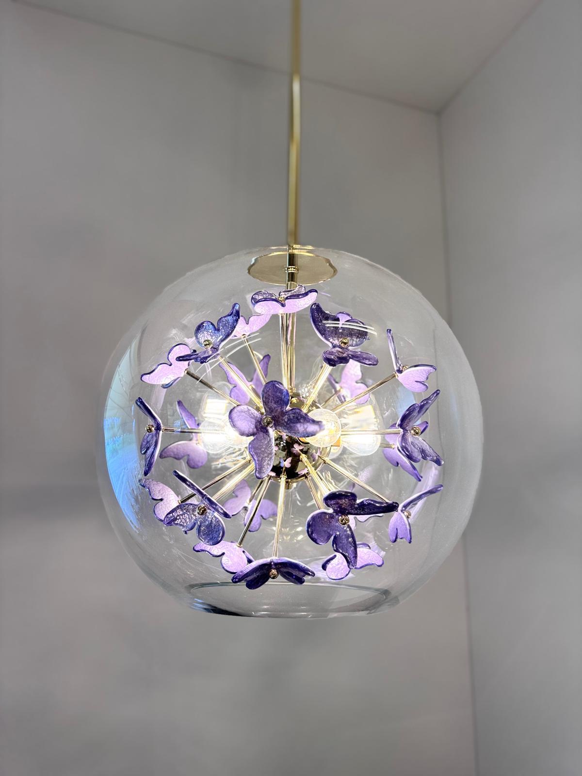 Ce lustre est unique par sa composition. Les fleurs en verre de Murano sont insérées à l'intérieur d'une boule en verre transparent ouverte dans sa partie inférieure. Il est suspendu par la tige en laiton et un baldaquin en laiton dont la longueur