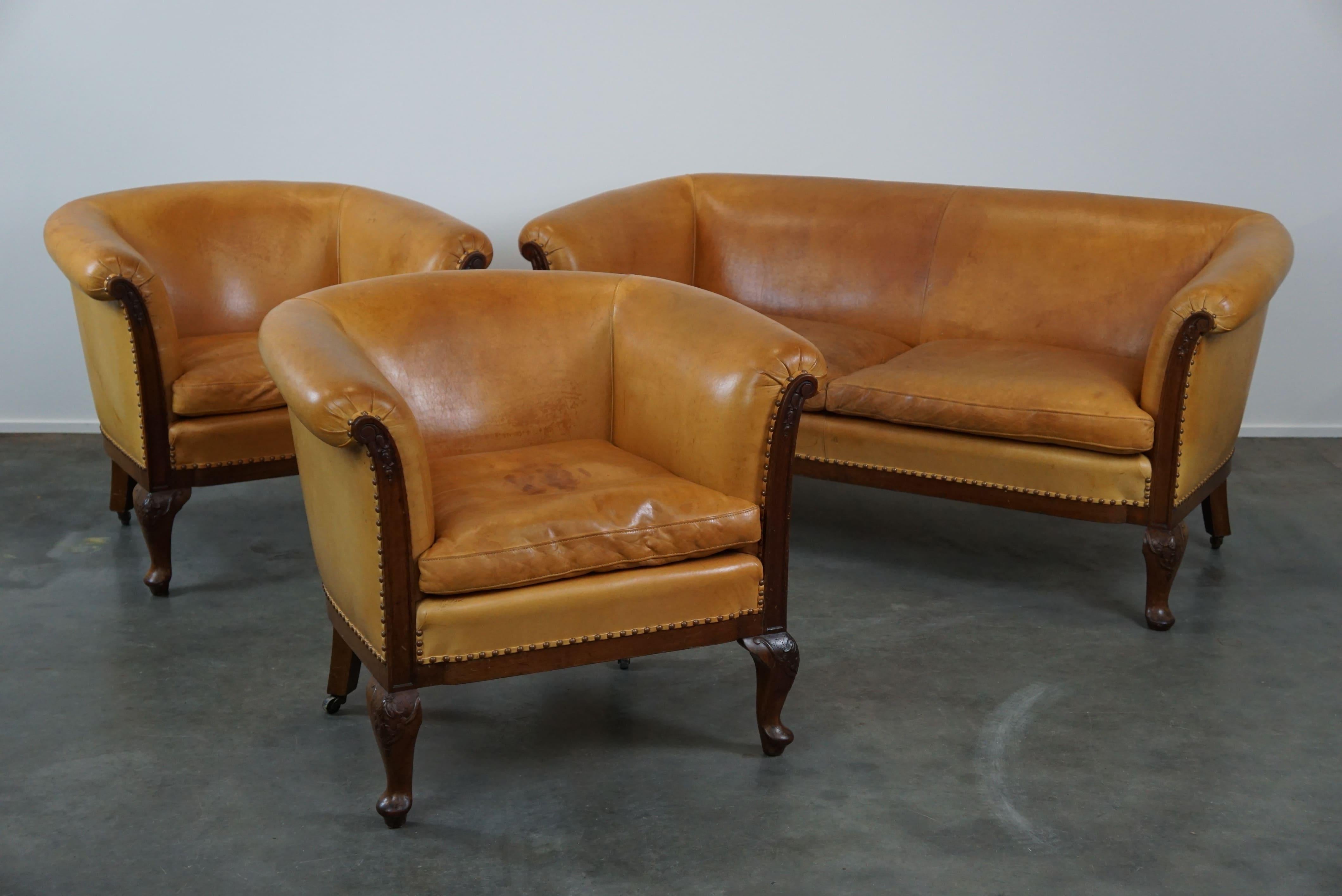 Offered: this unique old set of 2 club armchairs and a sofa in cognac-colored leather, featuring wood carvings, Queen Anne legs, and wheels on the back legs.

A unique opportunity for enthusiasts! Want a complete set? Then we have it here! This