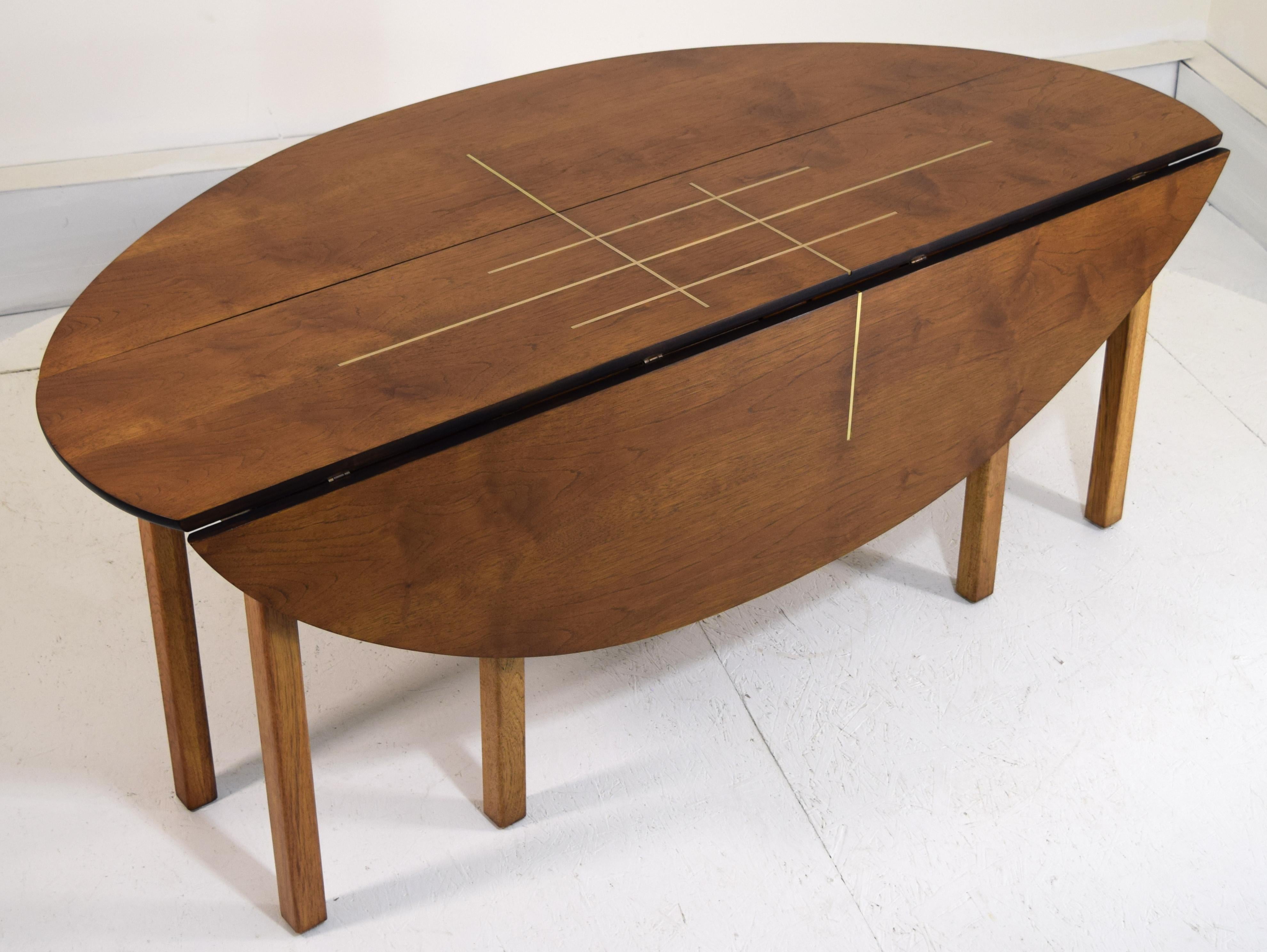 This gorgeous dining table was given a splash of brass inlay with a geometric pattern and entirely refinished with lacquer. The wood is a birch and the gate legs open to 2 possible positions to allow seating banquet style of 6. Outstanding condition