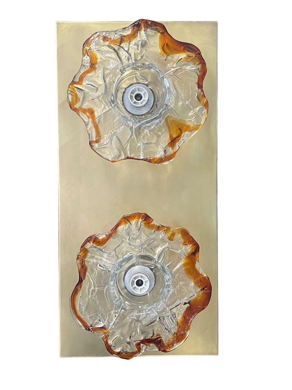 Une paire d'appliques en verre de Murano unique et saisissante, conçue par Mazzega, Italie, vers les années 1970. Chaque applique présente deux fleurs en verre de Murano soufflé à la main, transparentes au centre et aux bords ambrés, créant une