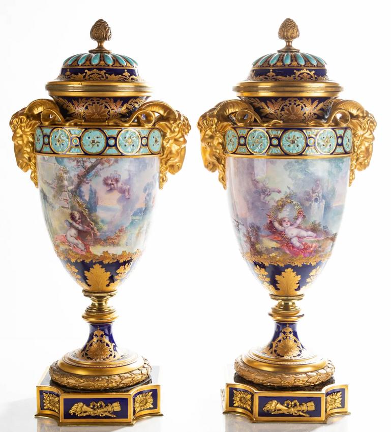 Deléitate con la grandeza del estilo Sevres con este magnífico par de urnas de porcelana pintadas a mano, un homenaje a la exquisita artesanía francesa de la Belle Époque. Las monturas de bronce dorado y el luminoso esmalte dorado muestran una