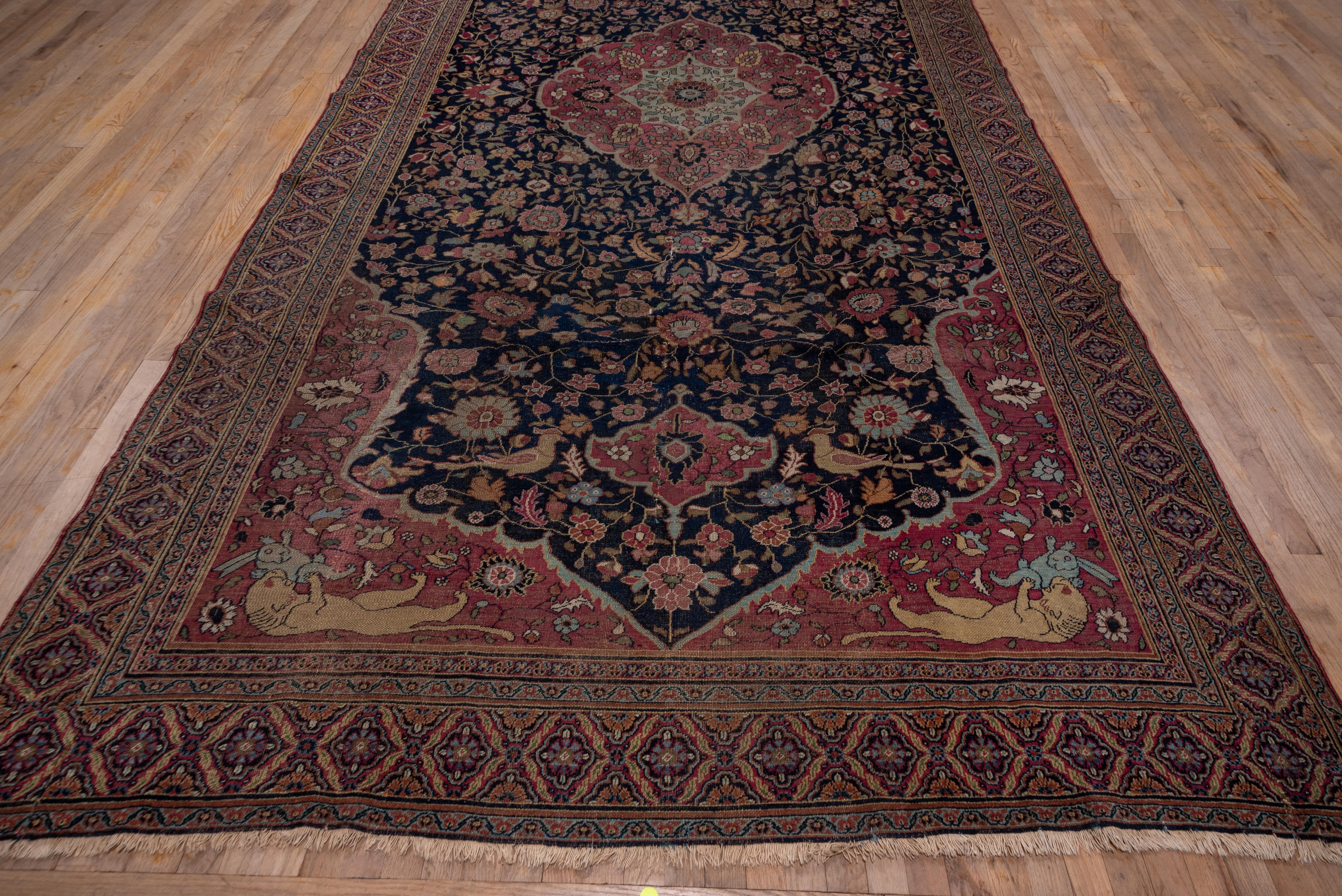 This antique northeast Persian carpet features a rose, gently lobed oval medallion with palmette accented central octogramme, set on a navy ground with birds, floral rinceaux and rose floating escutcheons. Lions pounce on hares in the rose field