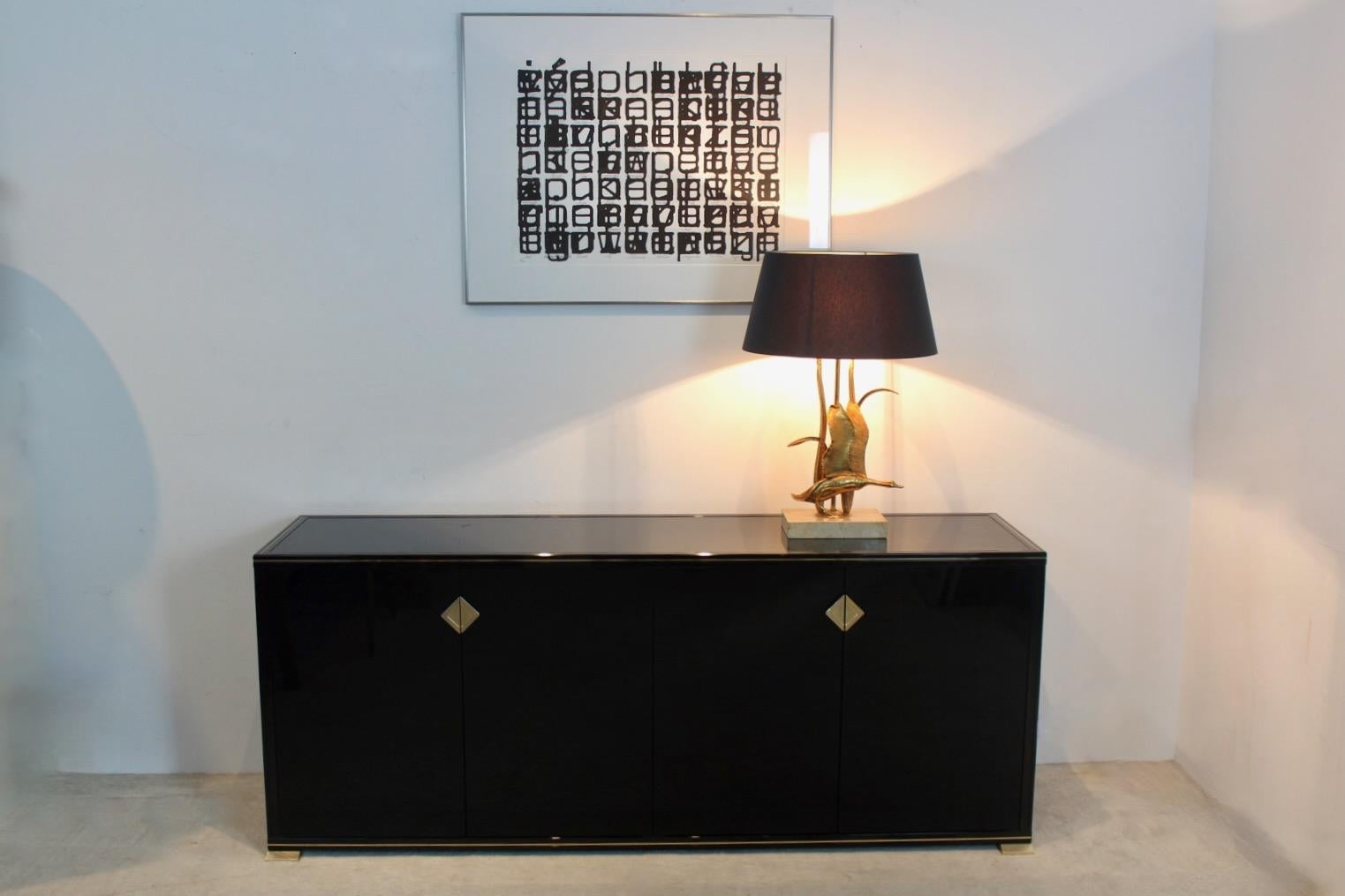 Unique Pierre Vandel Paris Black lacquered French Dressoir. In black lacquer with painted glass top and stylish gold trim and handles. The unit has four doors and two cupboards. 
With some light wear due to age and use, on the backside there is a