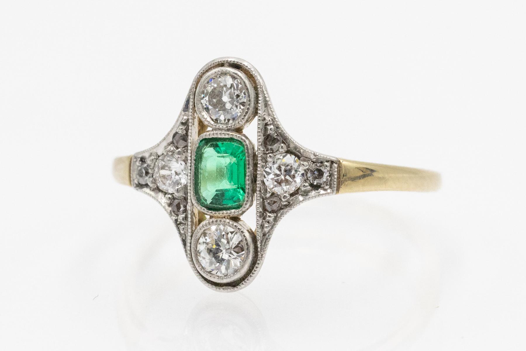 A charming ring crafted from 14-karat gold (0.585 fineness) and platinum (0.900 fineness). The ring is set with a central emerald weighing approximately 0.20 ct in a beautiful, intensely green color. Additionally, the ring is set with four old