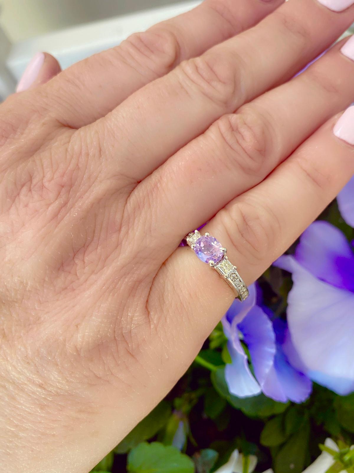 An extremely unique estate ring showcasing a remarkable center stone! The 14k white gold ring features a unique and vibrant purplish-pink oval-cut sapphire, weighing 1.37 carats, accented by 12 princess and round brilliant-cut diamonds weighing