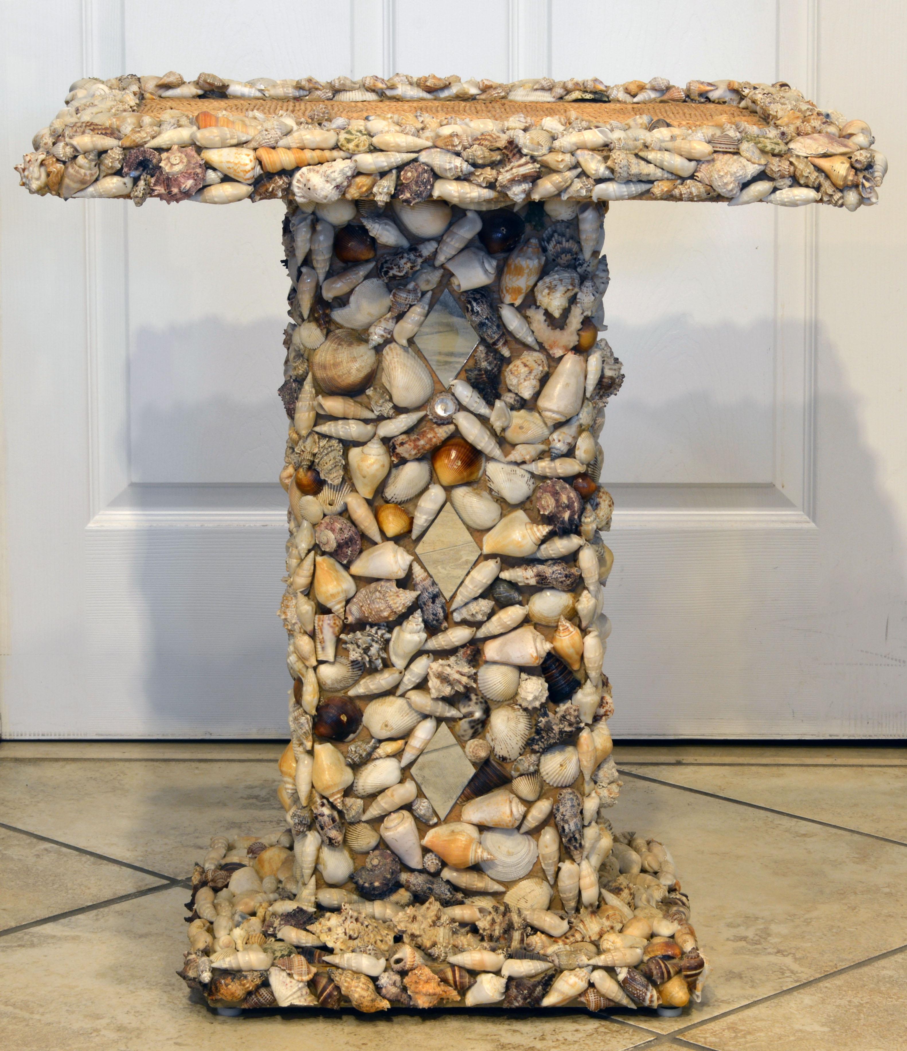 A unique sea shell and mirror encrusted pedestal accent table with the top of woven raffia. Well constructed of an inner core of particle board and quite heavy. Ideal for that beach ambiance or the room with maritime connotations.