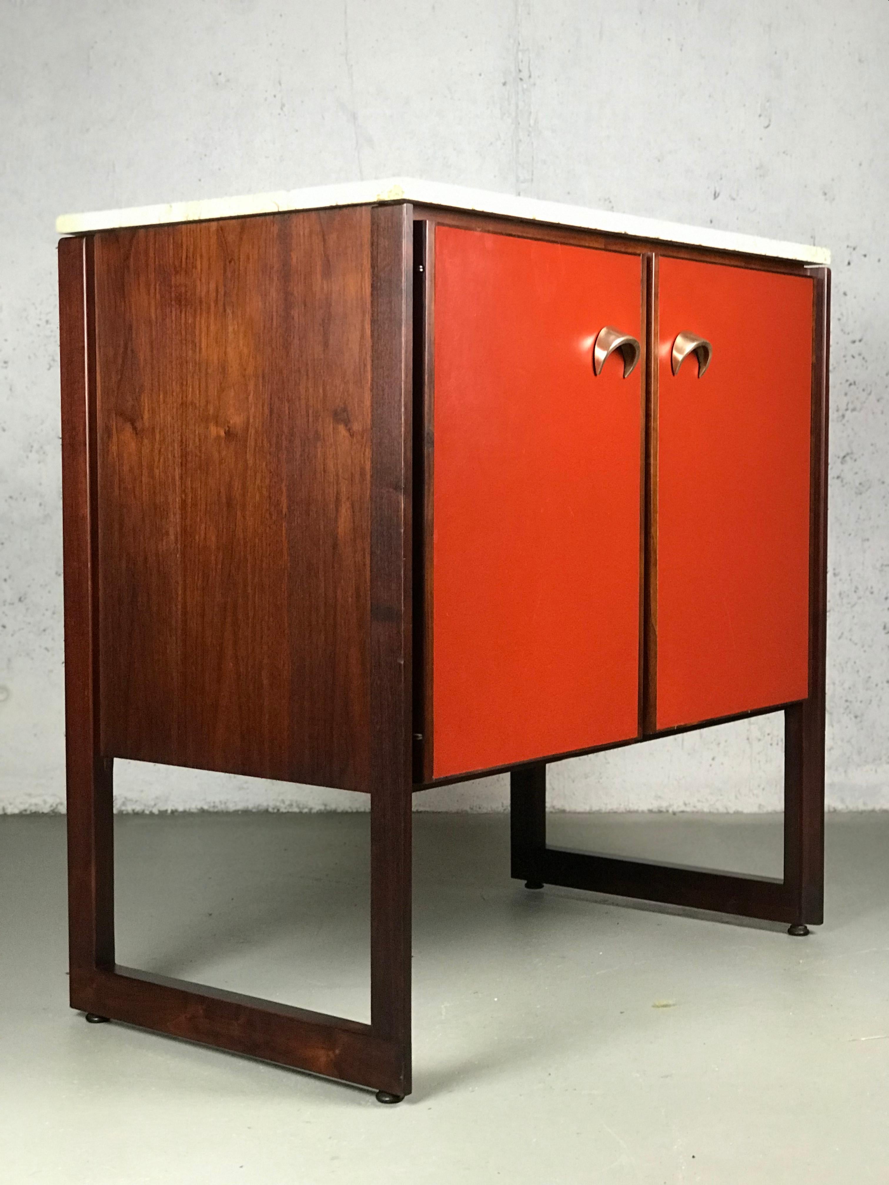 Wonderful example of American modernism by Jens Risom. This cabinet is made of an array of contrasting materials: walnut, rosewood, travertine marble, red vinyl and brass. Rosewood is used in the trim around the doors, framing pieces and legs. There
