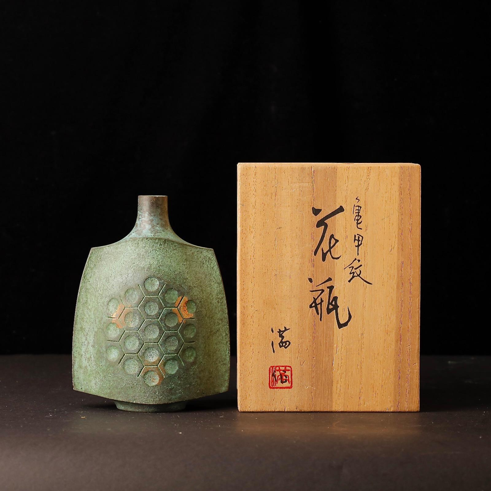 A striking and sculpturally refined Japanese bronze vase by artist Ohaka Mitsuru, crafted during the Showa period (20th century). This piece features an elegant and unusual silhouette with a gently curved body, finished in a deep green patinated