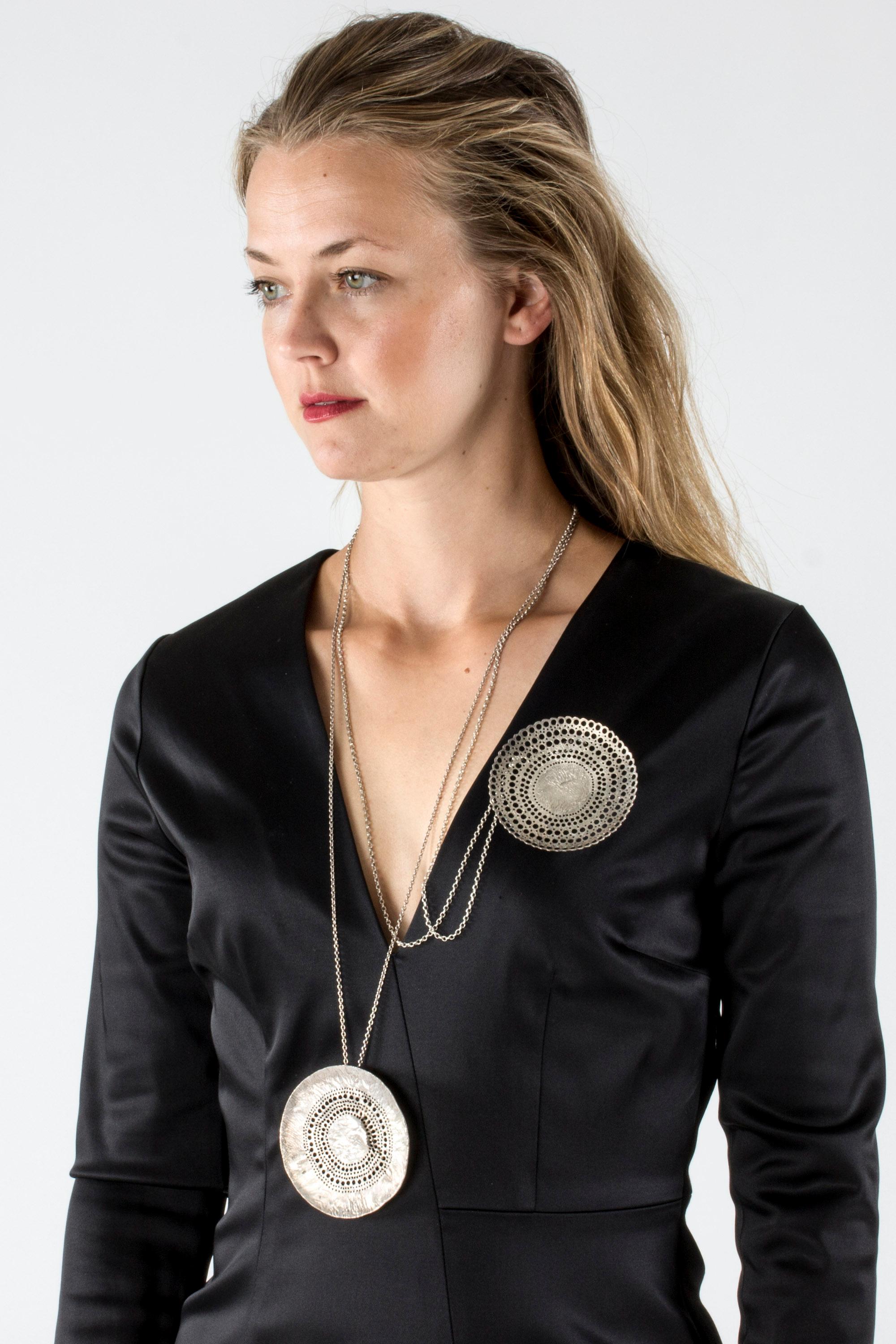 Large, round silver pendant by Liisa Vitali, in a captivating design. The surface has an undulating, organic surface. Different sized spheres form a circular pattern around the center of the pendant, creating a geometric contrast.

This necklace is