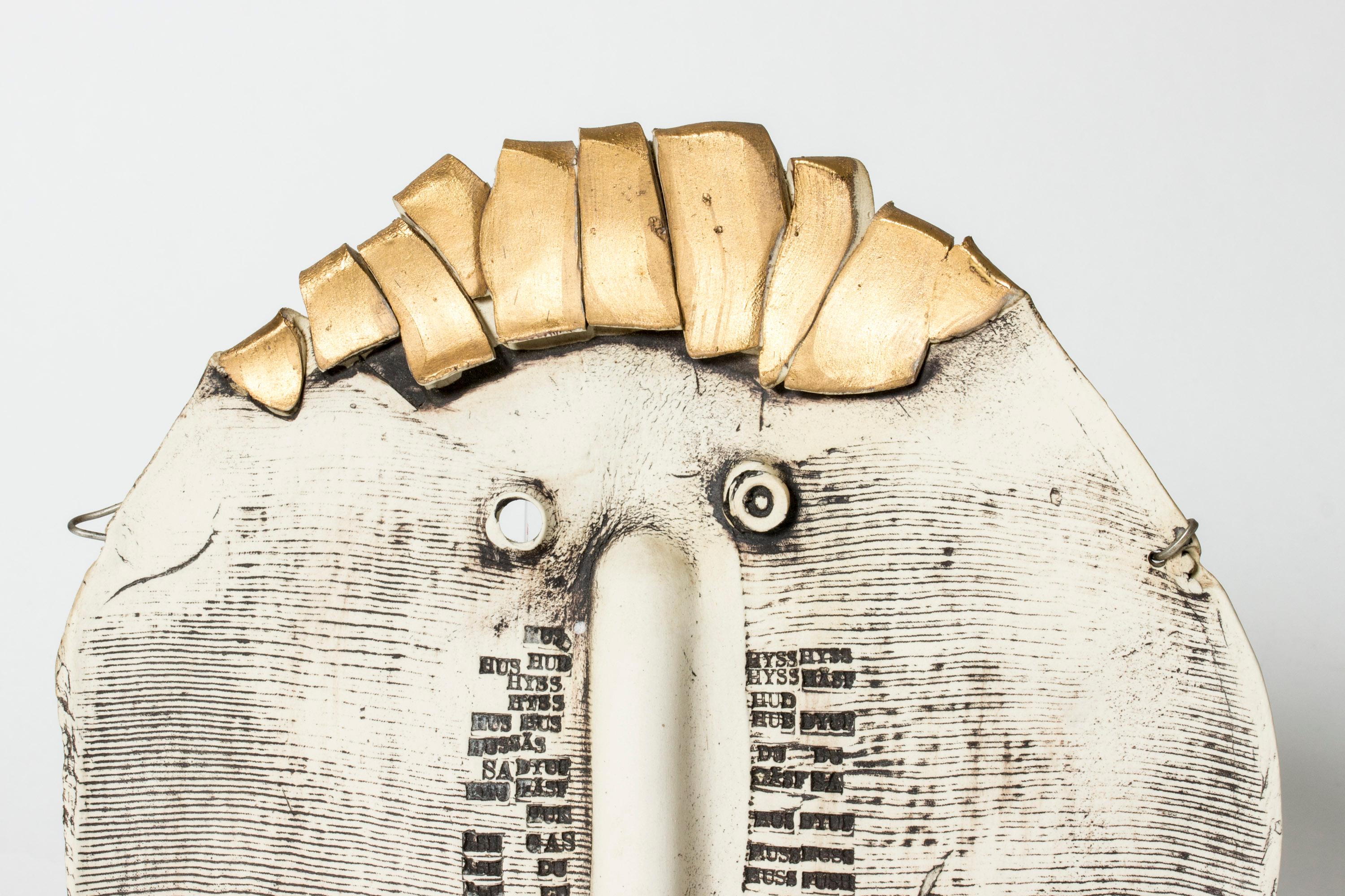 Striking, unique stoneware wall mask by Bengt Berglund. Abstract face form with a gilded top and enigmatic embossed pattern of letters.