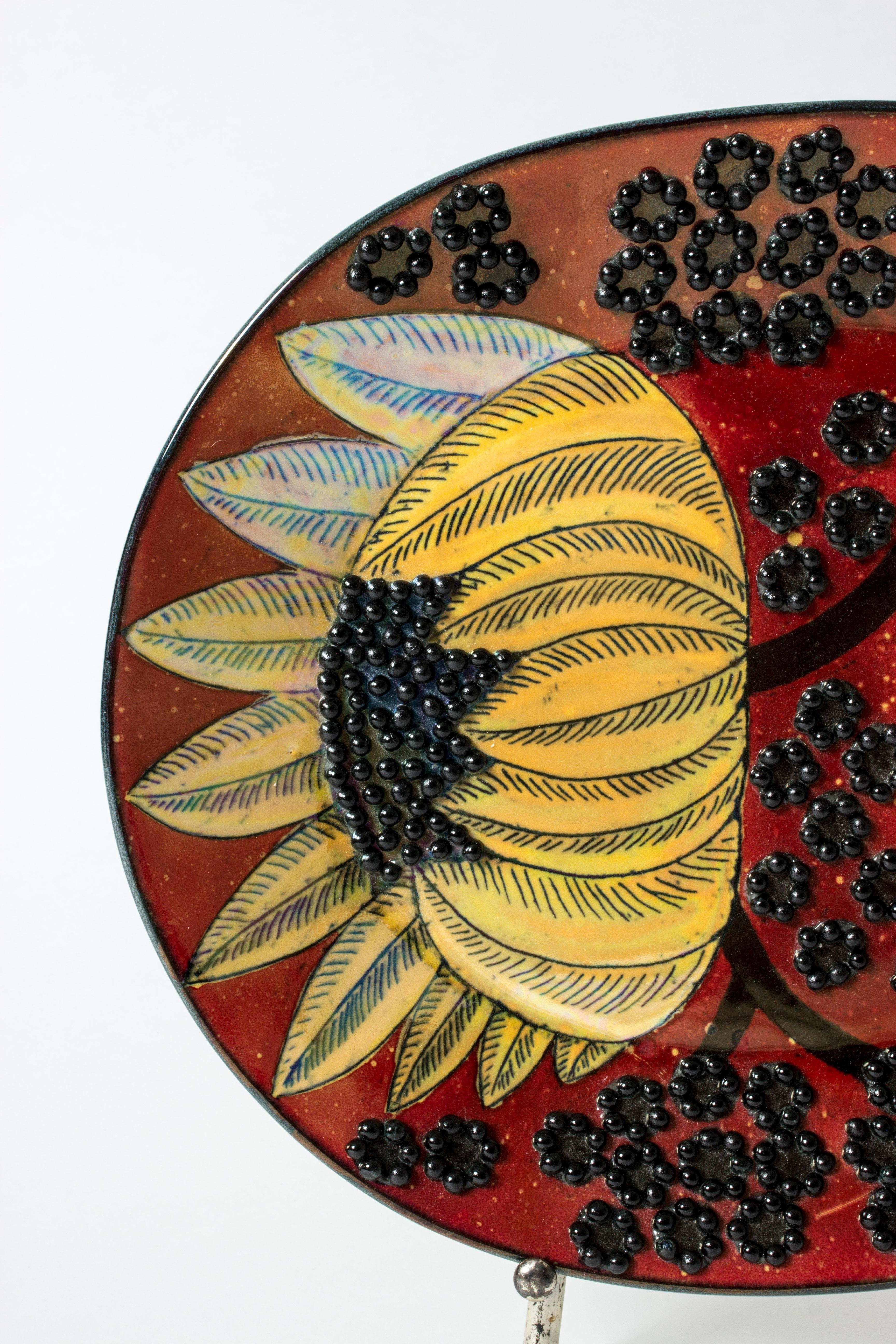 Amazing, unique stoneware platter by Birger Kaipiainen in an oval form. Beautiful composition of yellow sunflowers against a rich red background, surrounded by a pattern of round black seeds in relief.