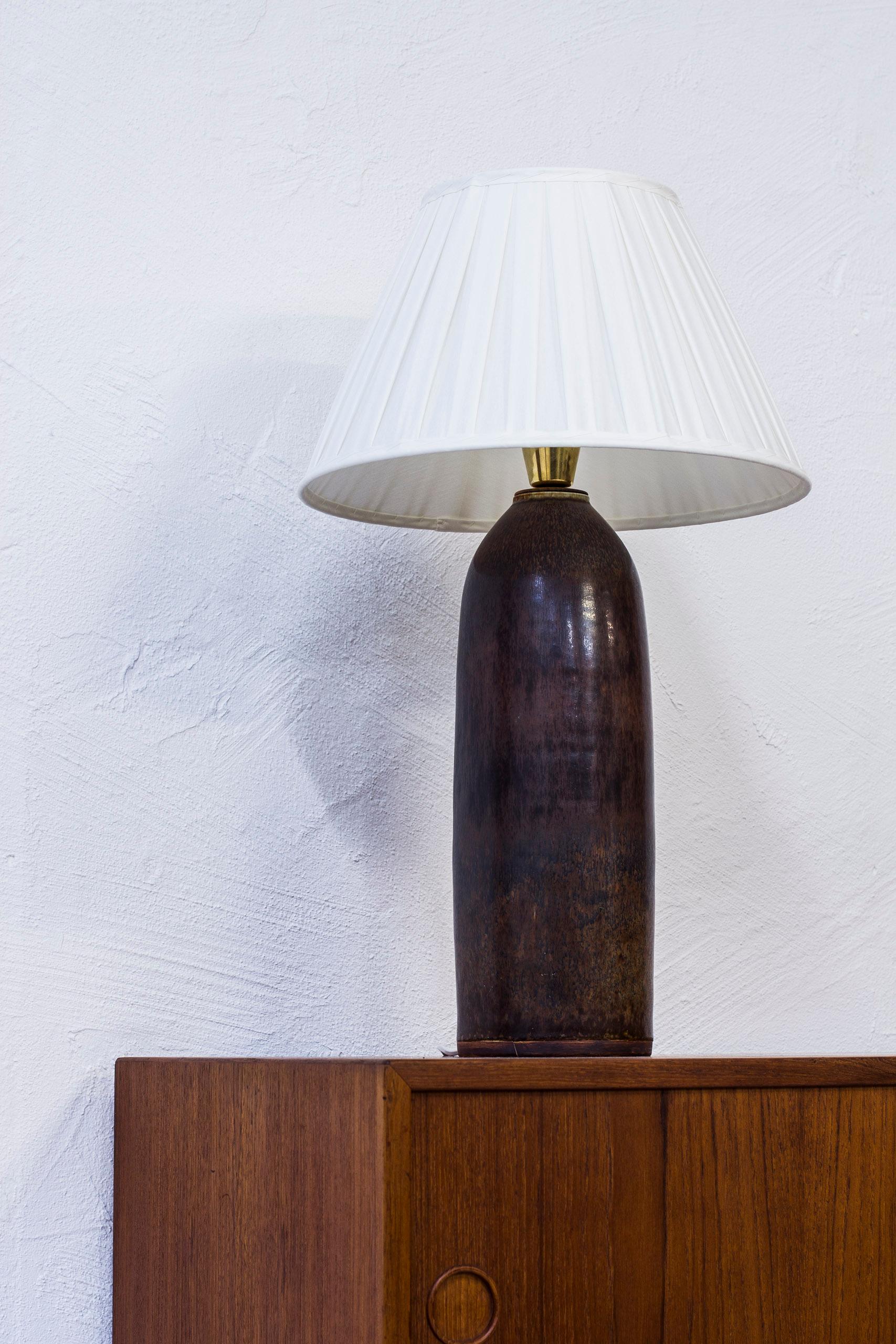 Table lamp designed by Carl-Harry Stålhane. Produced by hand at Rörstrand during the 1950s. Blue, grey glaze with hints of purple. Brass fitting on the top. With new hand-sewn, pleated chintz lampshade. Excellent condition with light age related