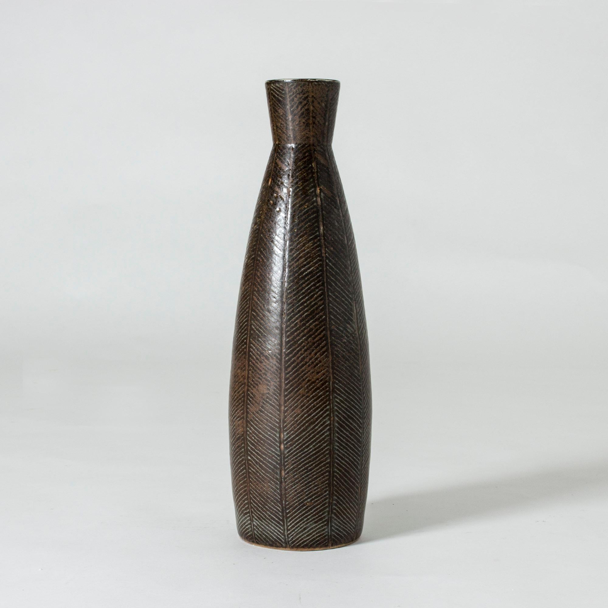 Unique floor vase by Carl-Harry Stålhane, made in chamotte stoneware with a dark brown glaze. A fishbone like pattern is etched onto the body, light colored semi translucent glaze is caught in the stripes.