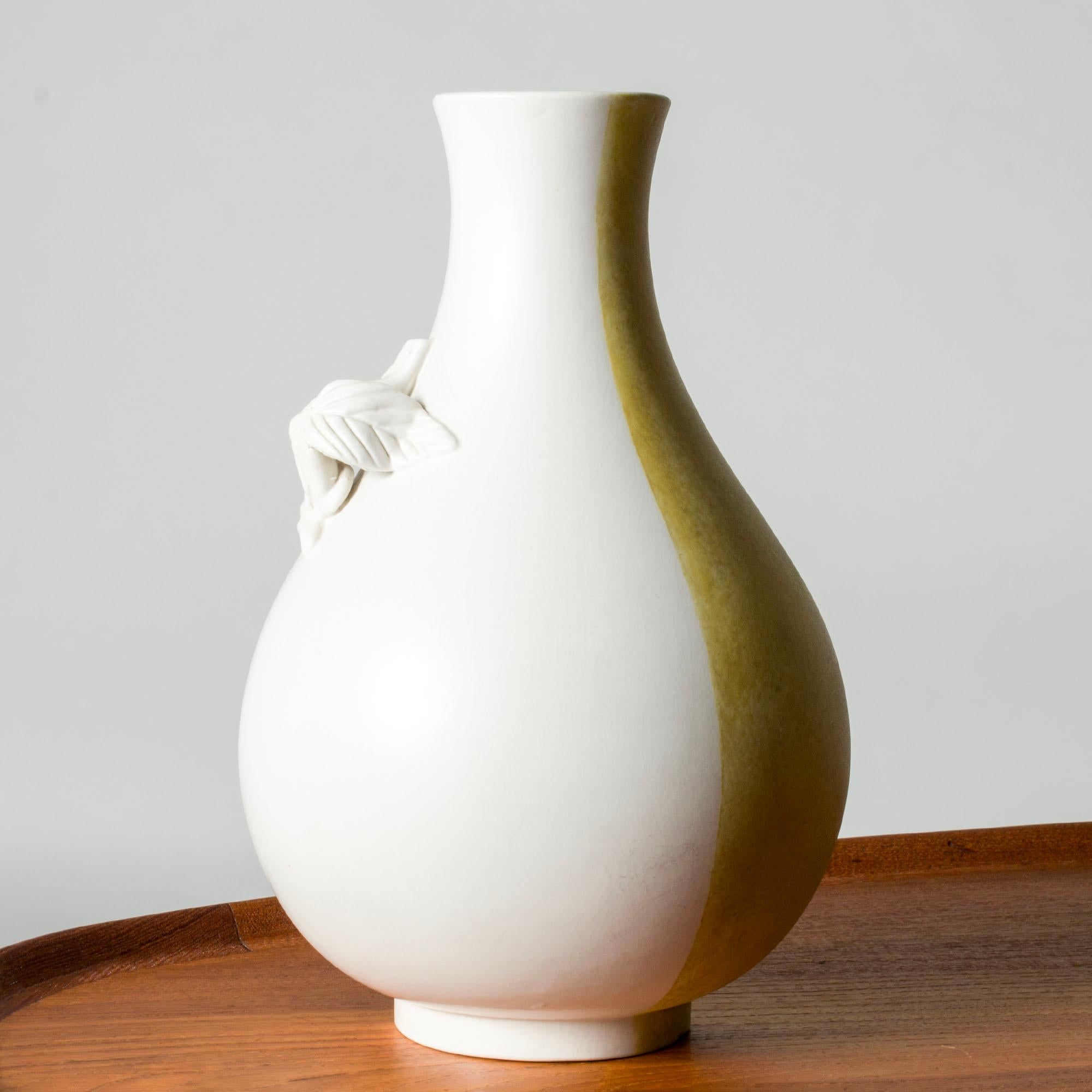 Unique “Surrea” vase by Wilhelm Kåge, in a captivating form of half a vase, decorated with an organic vine that contrasts with clean vessel. Glazed with white carrara glaze with brown and yellow decor.

The “Surrea” stoneware series was first