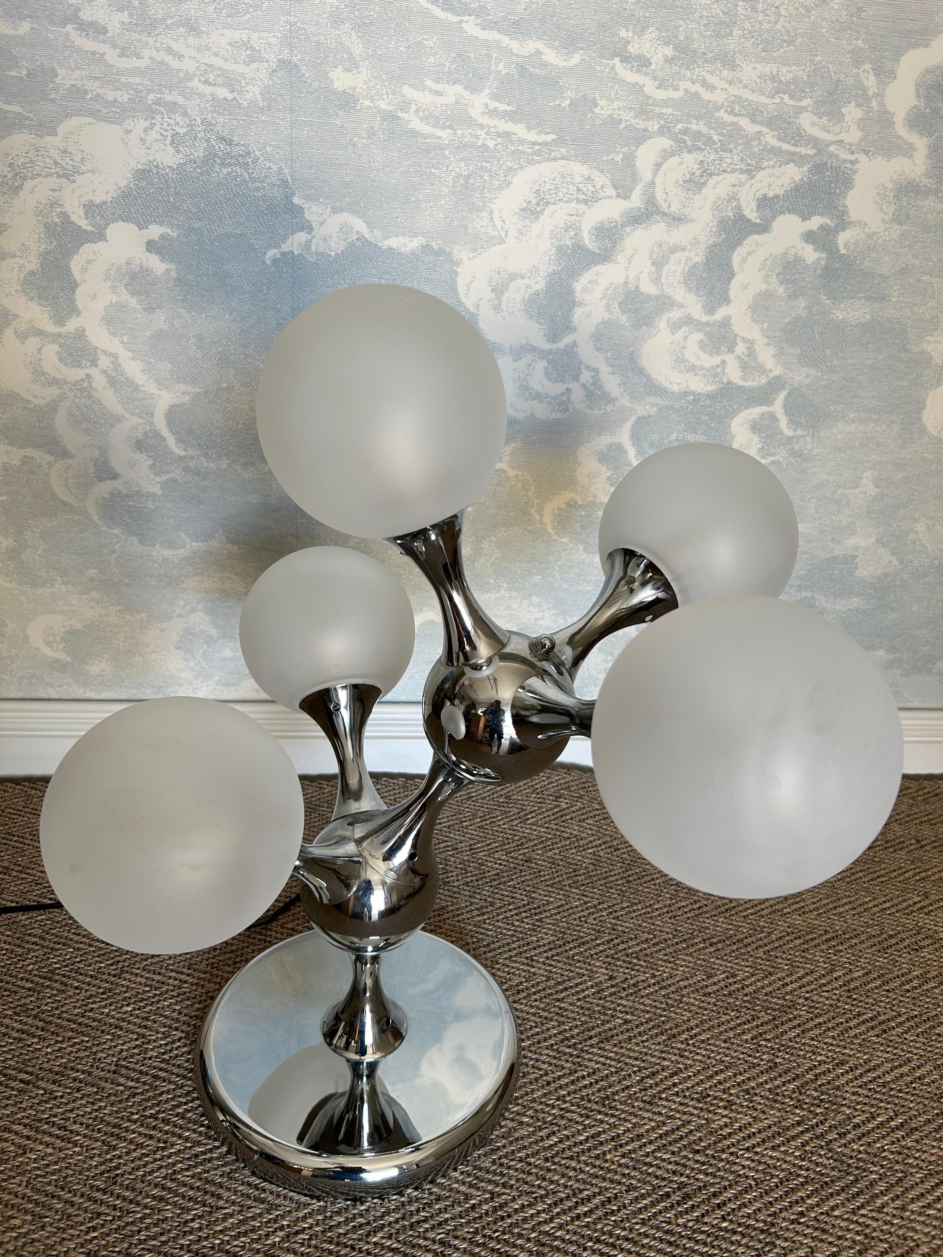 Cette lampe de table unique en son genre, en forme de molécule de chaîne de carbone, incarne l'énergie et le dynamisme du modernisme des années 1970 !

Contenant cinq sphères opaques, disposées autour de deux atomes centraux, le cadre chromé agit