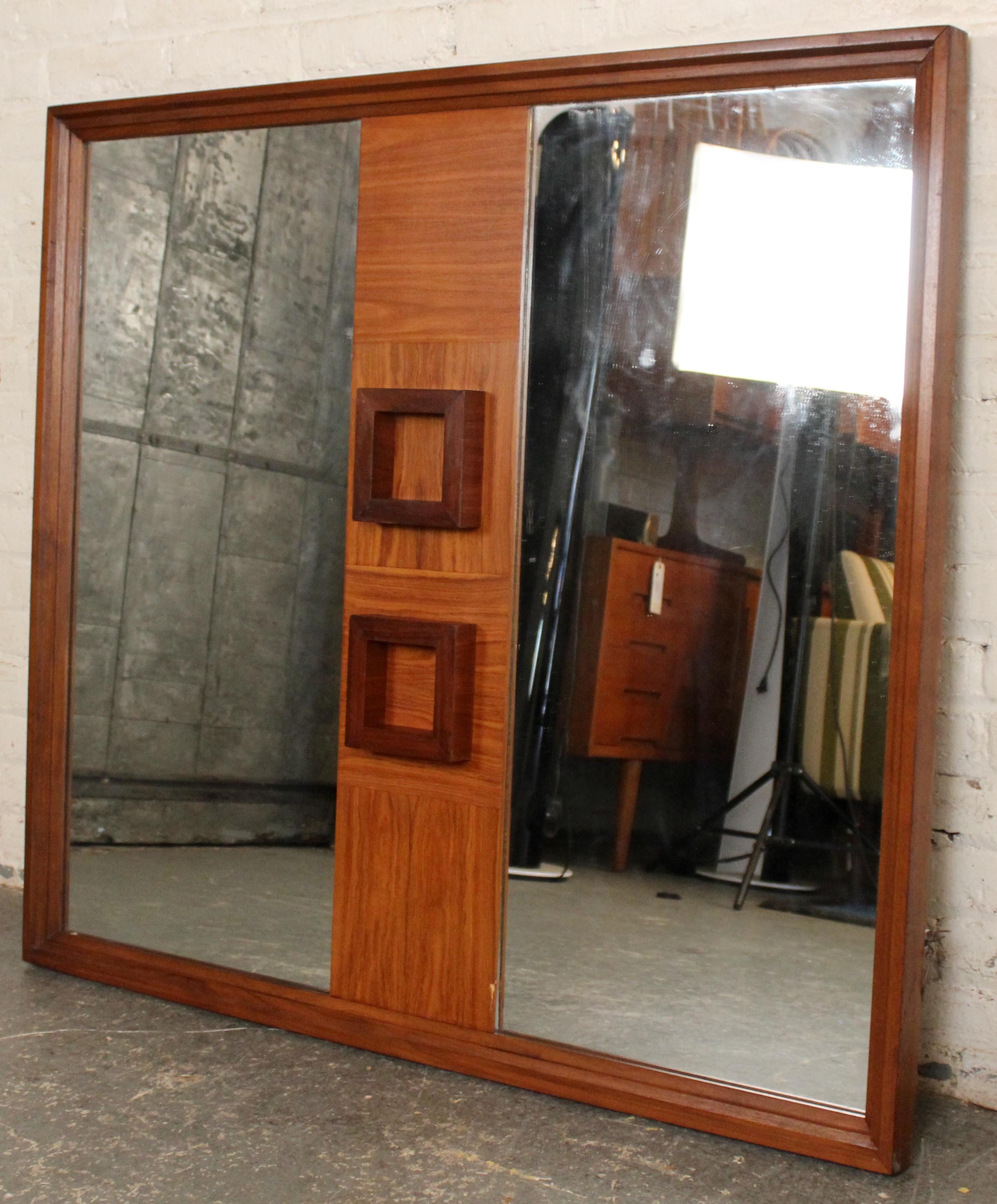 Striking Mid-Century Modern wall mirror featuring Brutalist design elements. The piece is framed in rich walnut with a distinctive center panel showcasing bold, sculptural square reliefs. Flanked by mirrored glass panels on either side, this mirror
