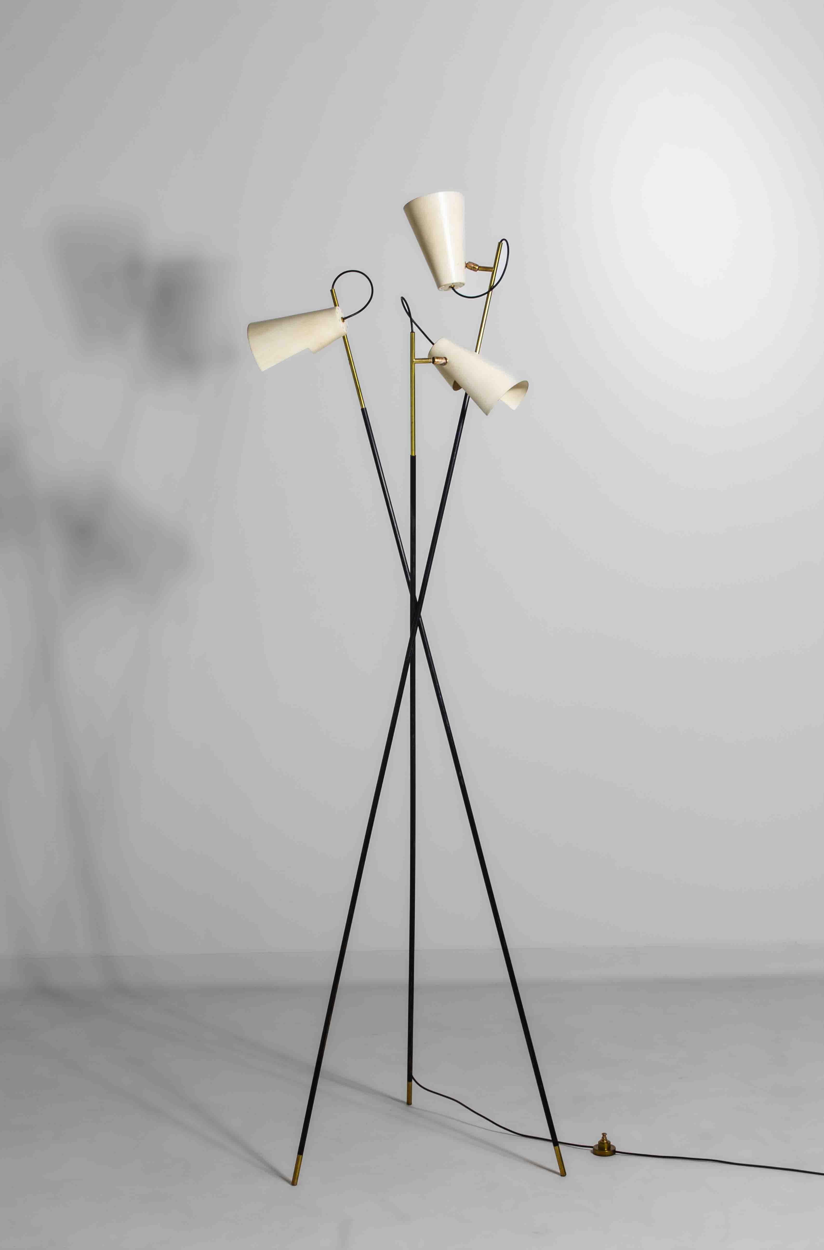 Elegant mid-century tripod floor lamp in the style of Stilnovo, made in the 1950s. It features three slender black legs with brass detailing and white adjustable metal shades. Each cone-shaped shade can be rotated to direct the light where needed.