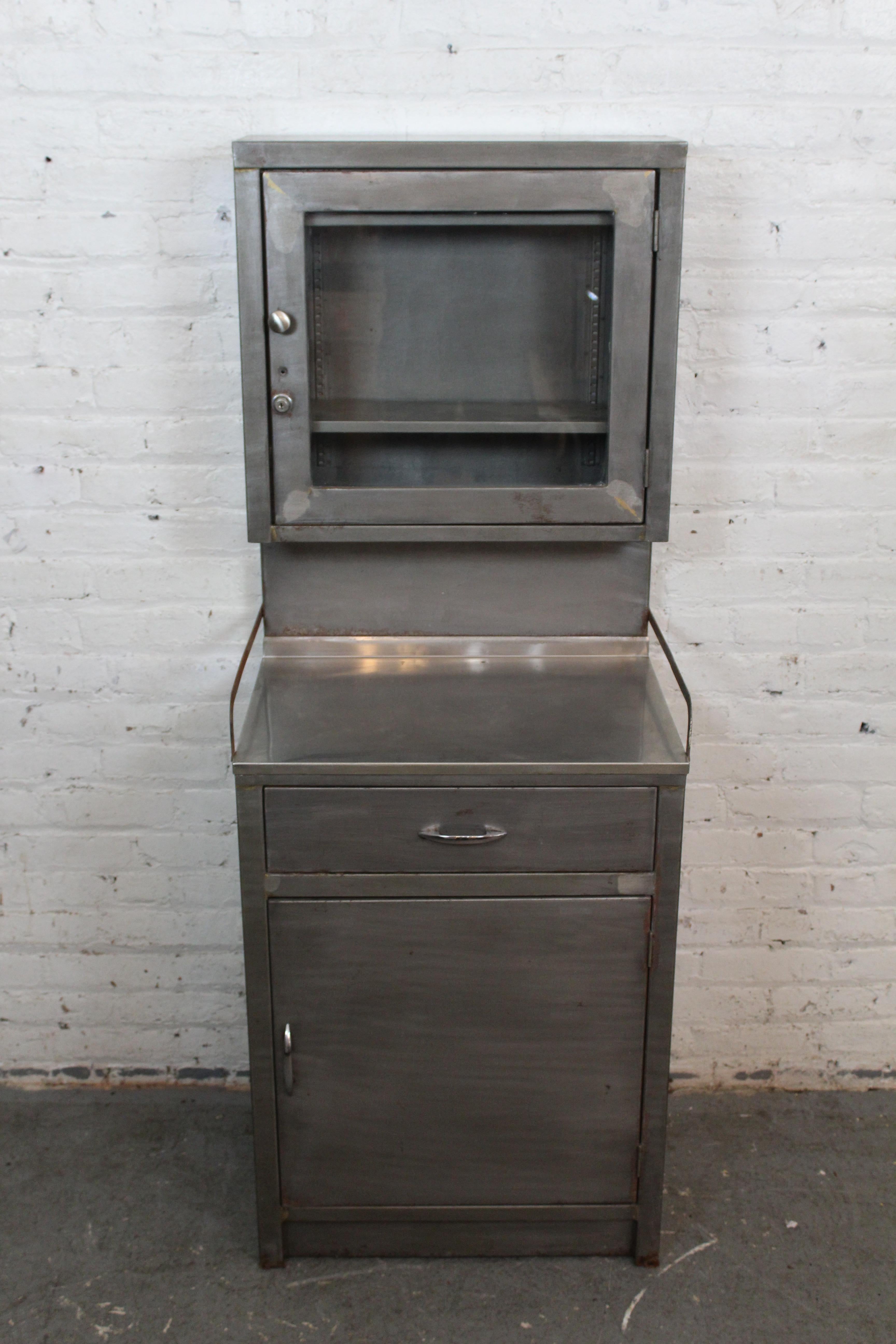 Apportez à la maison l'aspect pratique unique de l'ère industrielle de l'Amérique avec cette huche vintage en acier inhabituelle ! Cette armoire à étages, d'un encombrement réduit de 2'x2', se compose d'une vitrine supérieure élancée avec une paire
