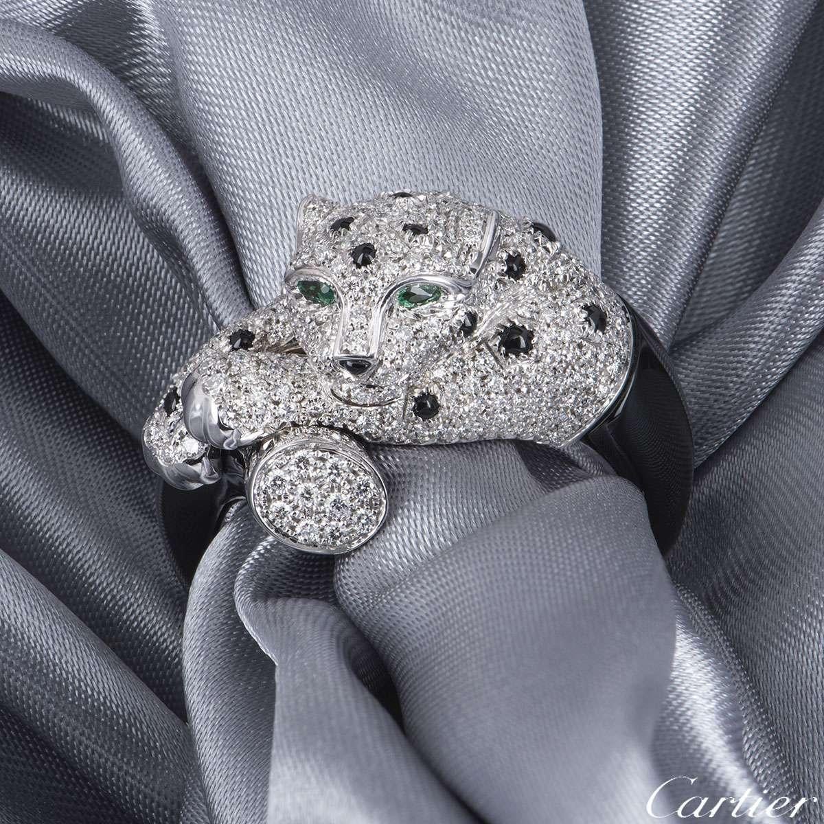 An extraordinary 18k white gold diamond and onyx ring from the Panthere de Cartier collection. The Panther is set with pave round brilliant cut diamonds with spots of onyx scattered on the body and has two emeralds set as the eyes. There are 292