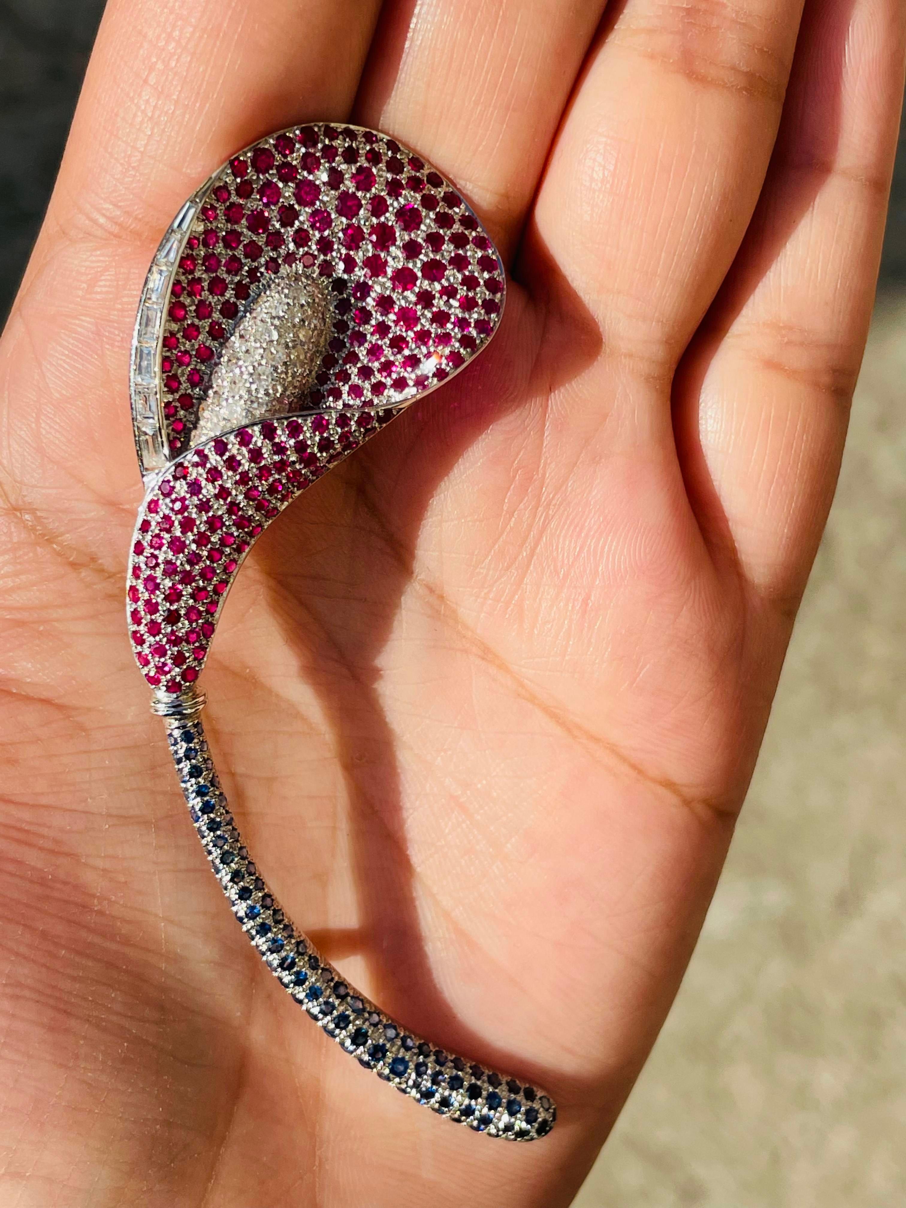Broche unisexe en or blanc 18 carats, ornée de rubis, de saphirs et de diamants, qui est une fusion de surréalisme et de pop-art, conçue pour faire une déclaration audacieuse. Fabriqué avec amour et dans le souci du détail, il comprend 6,3 carats de