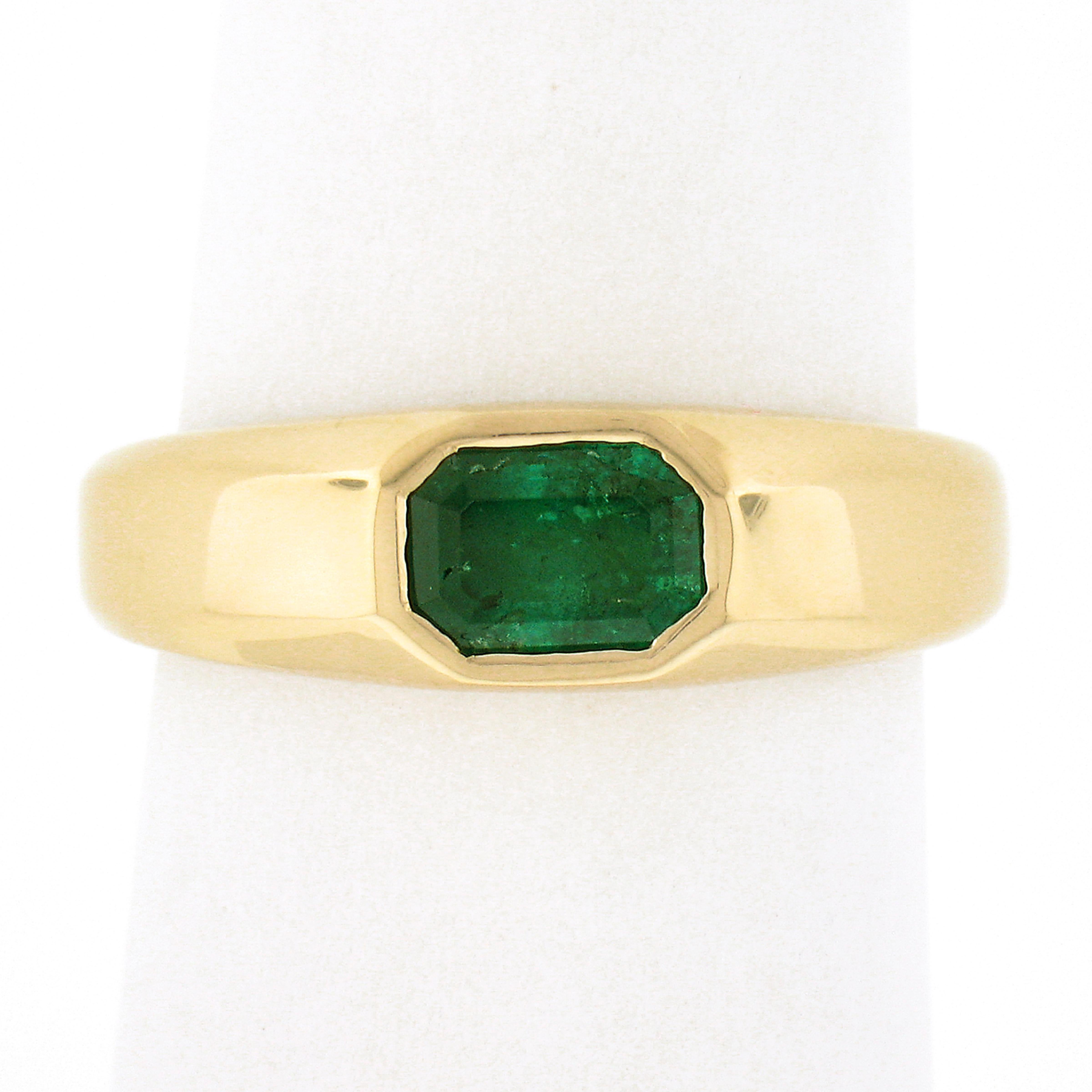 Here we have a simple, yet absolutely gorgeous, emerald solitaire ring that is newly crafted from solid 14k yellow gold. The solitaire is elongated emerald cut and is neatly bezel set sideways at the center of the ring, This well-made and super