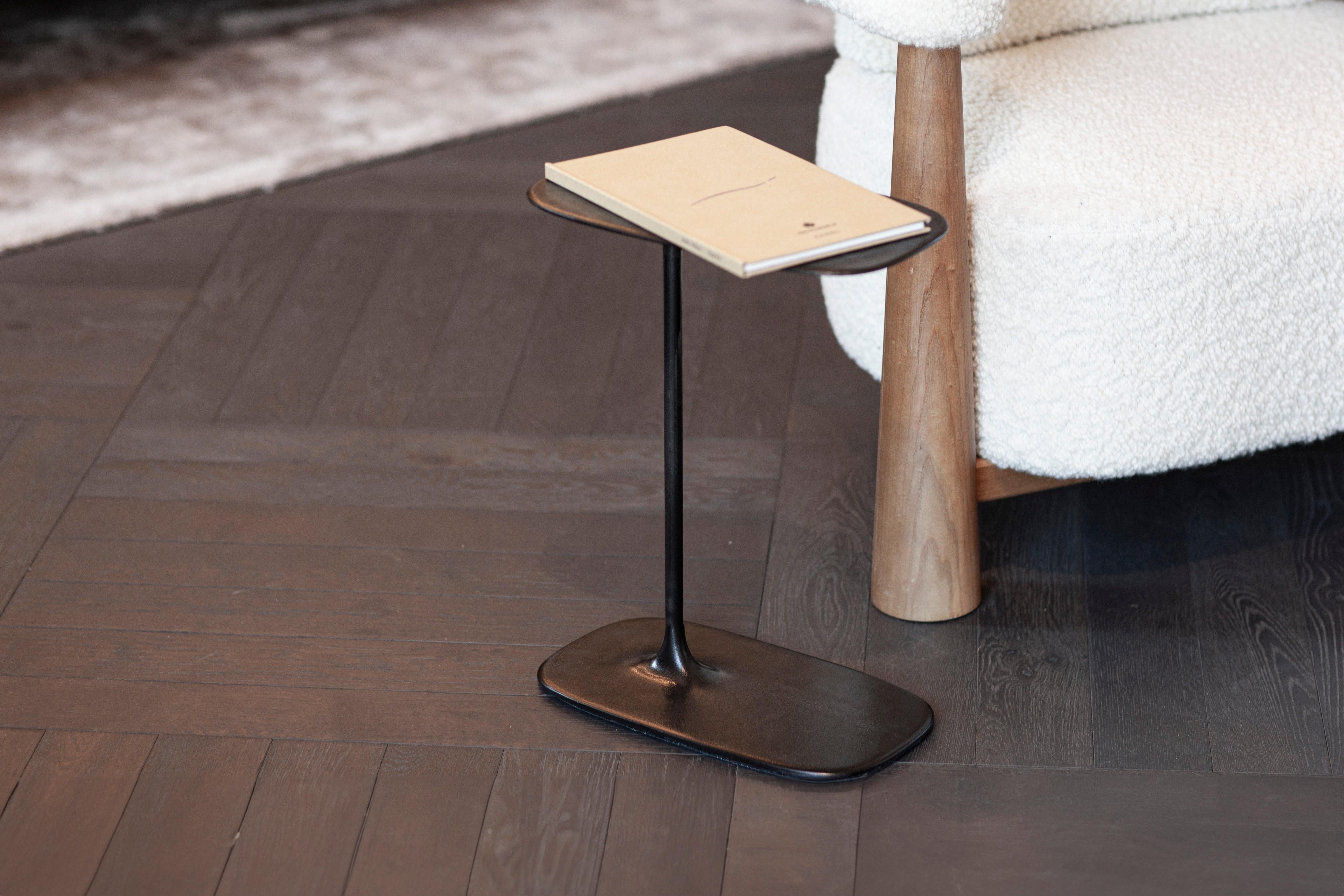 The Fluid Low Side Table, crafted using the sand-casting method and standing 47 cm tall, is perfectly proportioned to sit beside your sofa. This compact table is an ideal companion for holding books, plants, or other essentials, complementing your