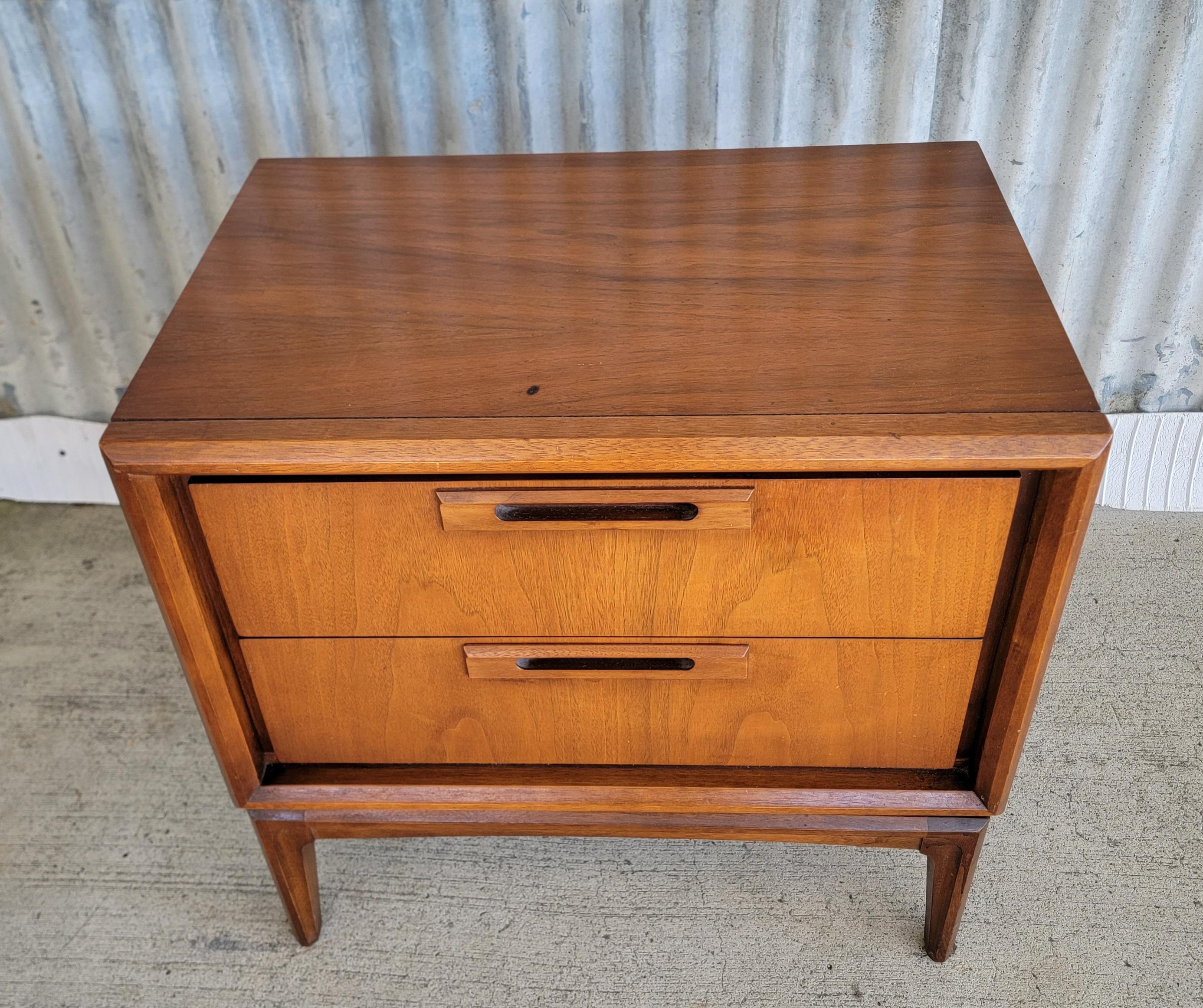 A walnut nightstand by United Furniture Company, circa. 1950. Fine craftsmanship with solid oak interior woods and dovetail construction. Dust panels between drawers and center drawer glide tracks. Very good original condition retaining its original