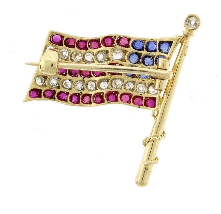 An 18 karat yellow gold  ruby diamond and sapphire antique American flag pin. The handmade flag pin is ¾ of an inch wide and 1 inch high and features 22 rubies weighing .50 carats 9 sapphires weighing .50 carats and 16 diamonds weighing .25 carat,