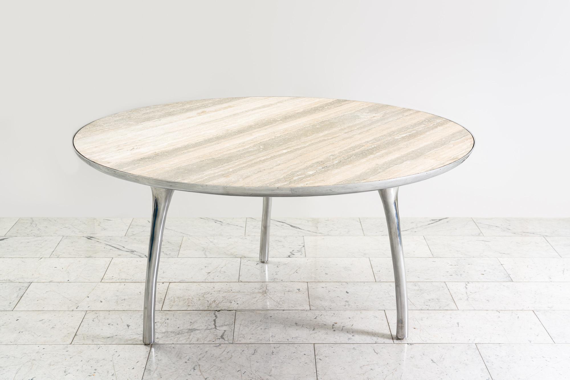 Alex Roskin’s dynamic indoor / outdoor Universal Dining Table, has a gracefully slim profile with three meticulously balanced aluminum legs supporting a travertine top inset into a sleek bezel. The minimalist design and Roskin’s penchant for precise