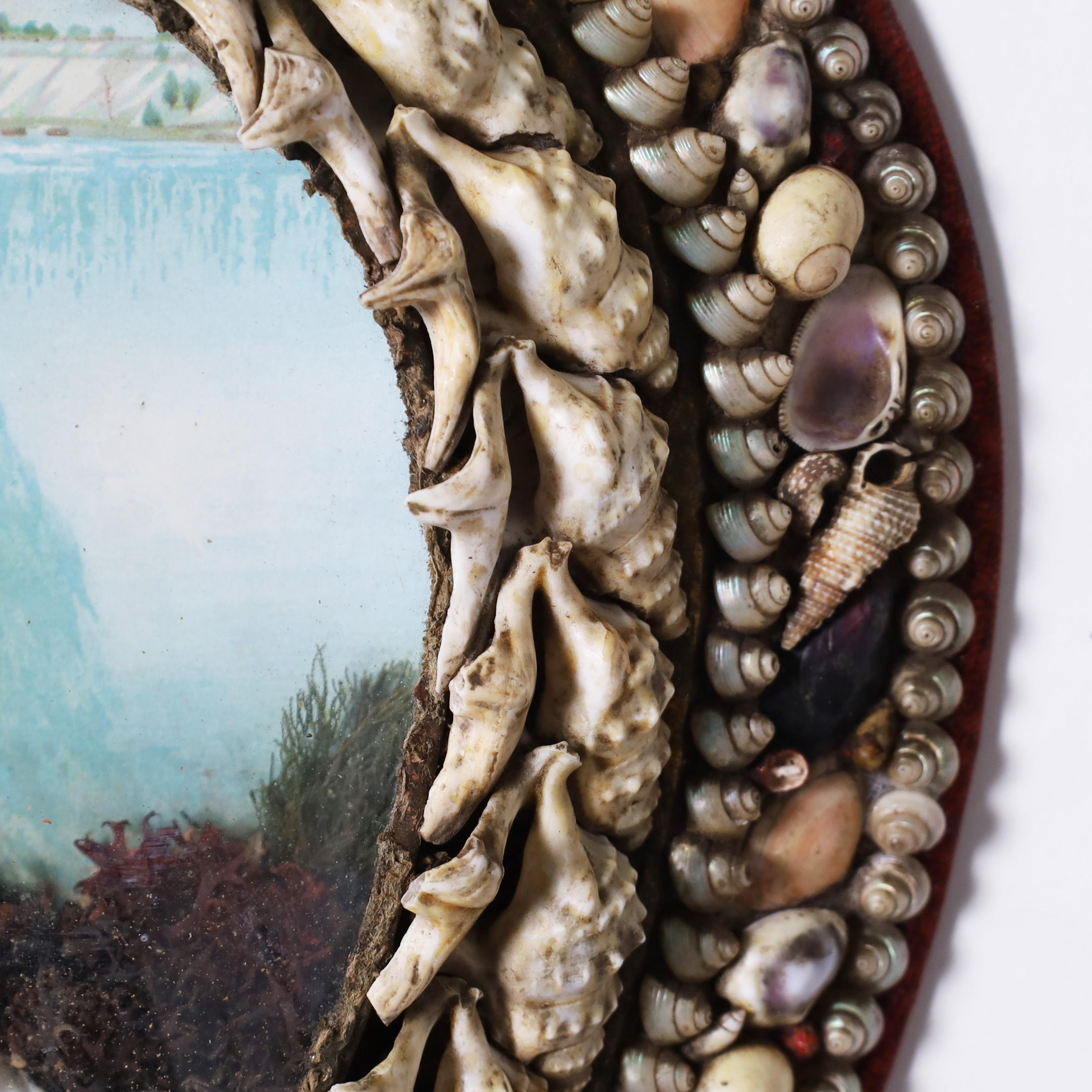 Charming antique sailors or honeymoon valentine with an unusual horse shoe form ambitiously decorated with exotic seashells around a convex glass lens decorated on the inside with shell and pink coral against Niagara Falls. 