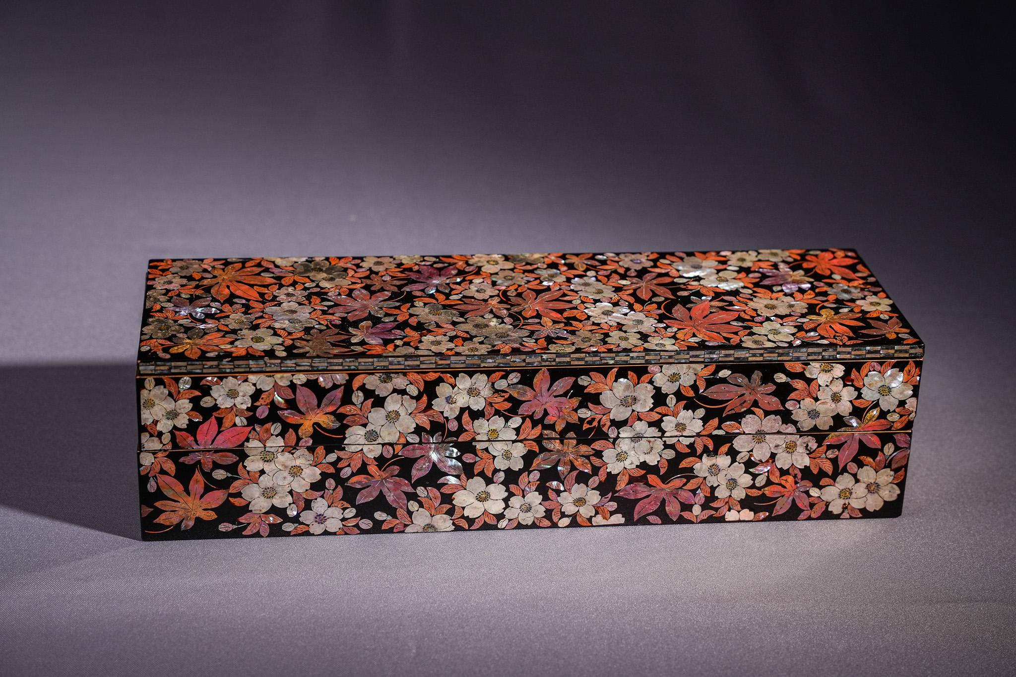 Die Raden Rectangular Box ist eine raffinierte Holzkern-Lackware, die in der Meiji-Zeit hergestellt wurde. Seine Oberfläche ist mit schwarzem Lack überzogen und reich mit dichten floralen Motiven in Raden-Technik intarsiert. Weiße Blüten und