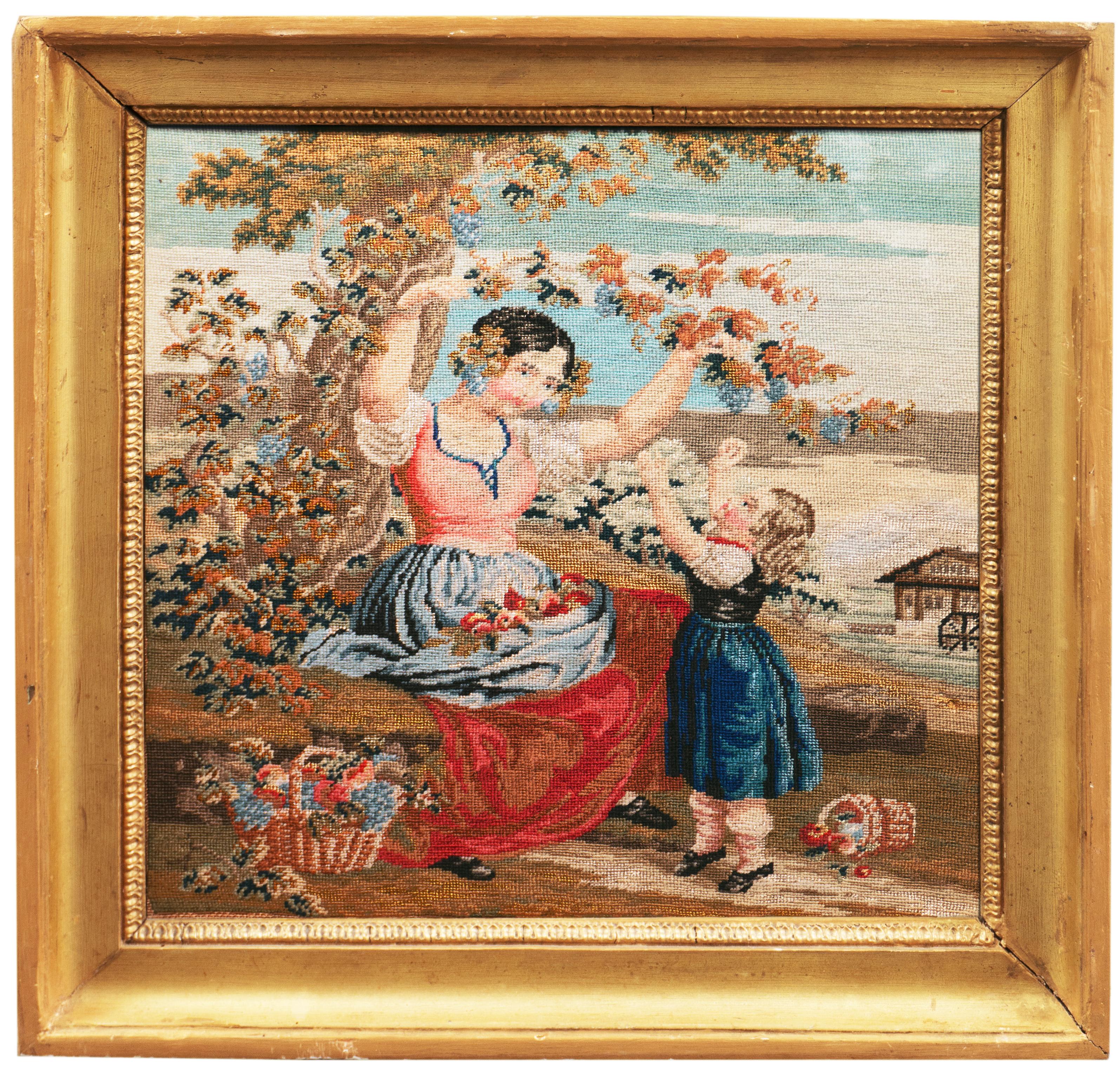 An unusually fine and delicate, mid-19th American figural needlepoint showing an idyllic view of frontier life with a young girl reaching up on tiptoes towards a grape-laden vine on a tree bough that her mother is lowering within her reach. A