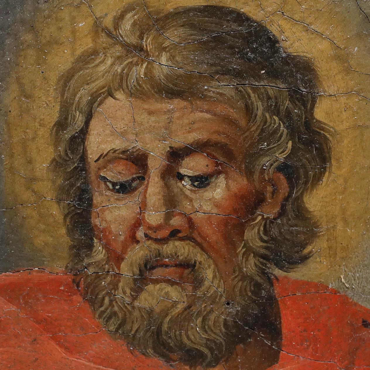 A devotional portrait depicting a bearded male figure with downcast eyes, likely a saint or apostle. The subject is shown in a red robe against a softly gilded background. Presented in a painted wood frame with green inner moulding and striped outer
