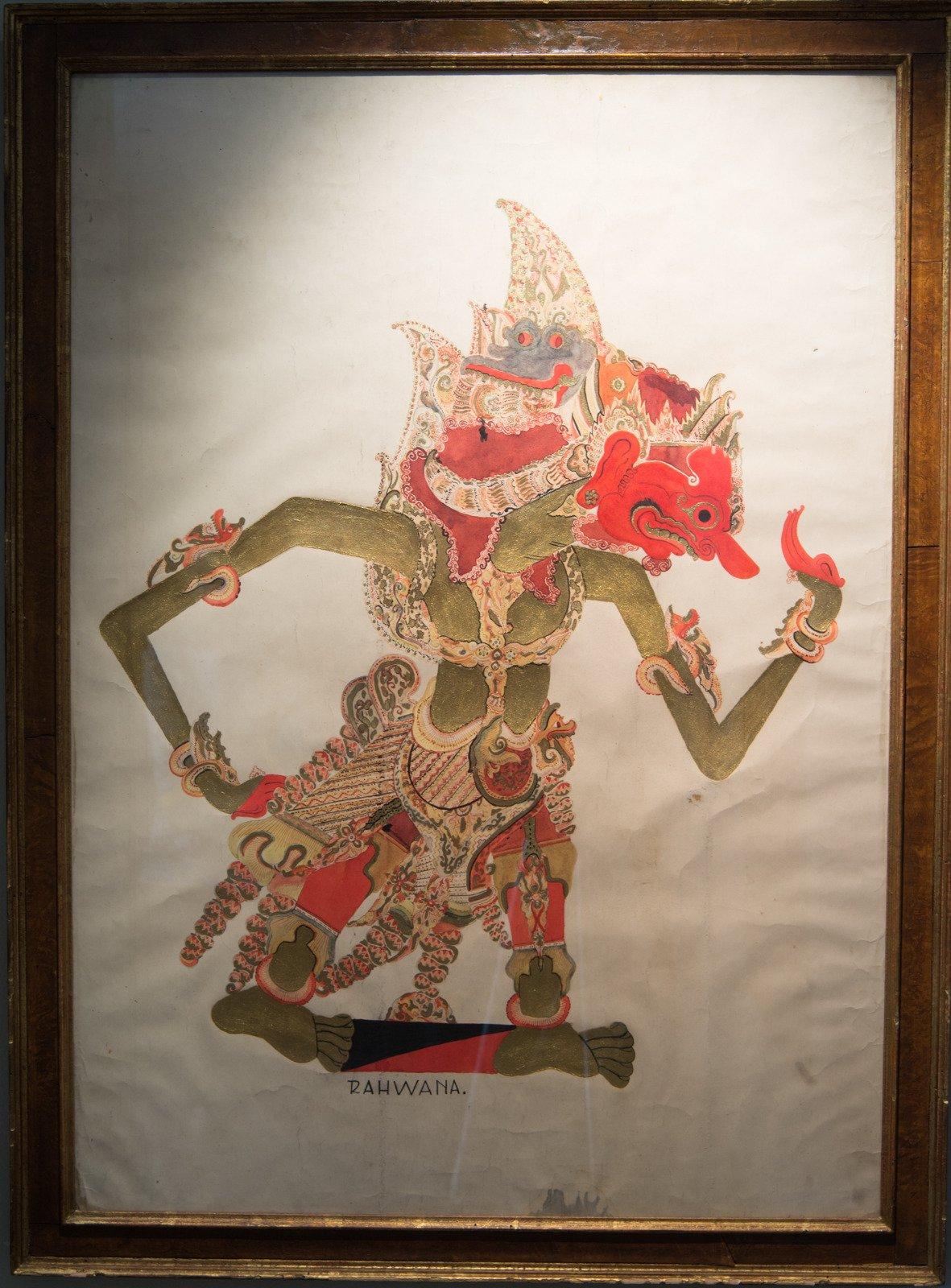 Pair of paintings on paper depicting wayang kulit also known as shadow puppets. These Indonesian folk paintings are on paper under glass with lovely aged burled wood frames. The paintings are likely early 20th century and frames are most certainly