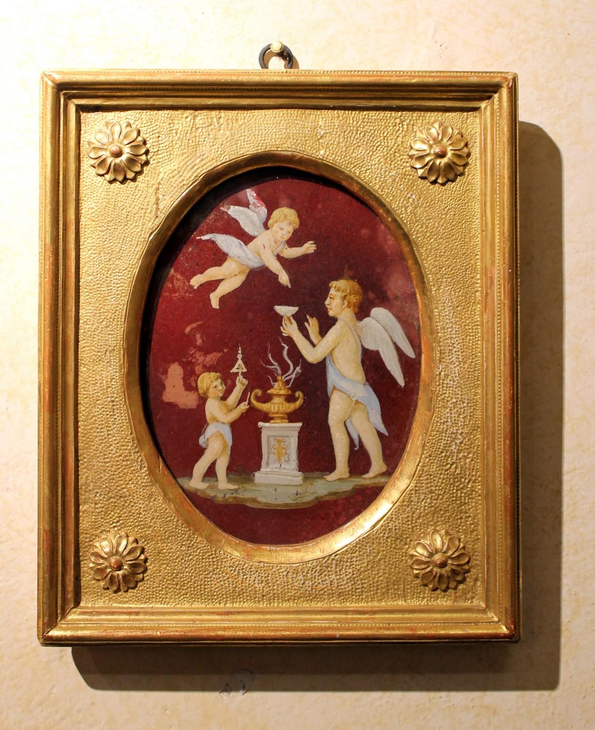 This lovely turn of the century Italian oil painting on glass features a Neoclassical scene with putto. 
The  winged cherubs and the architectural elements are rendered in soft pastel tones while the background is red. Both the color palette and the