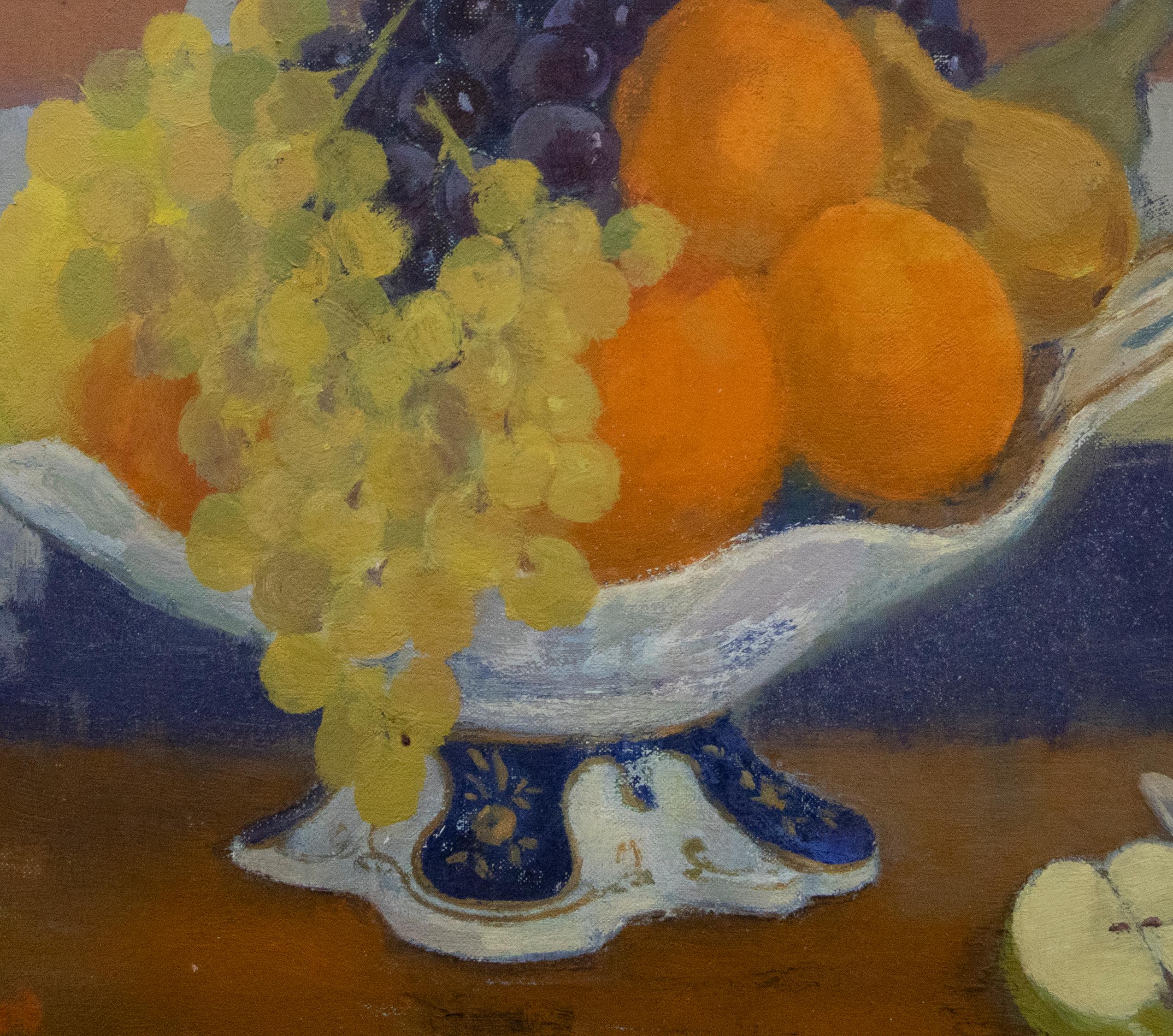 Nature morte moderne et colorée d'une coupe à fruits en porcelaine remplie à ras bord d'oranges, de poires, de pommes et de raisins. Au premier plan, une pomme coupée et un couteau se trouvent à droite du bol sur socle, ce qui donne de l'ampleur et