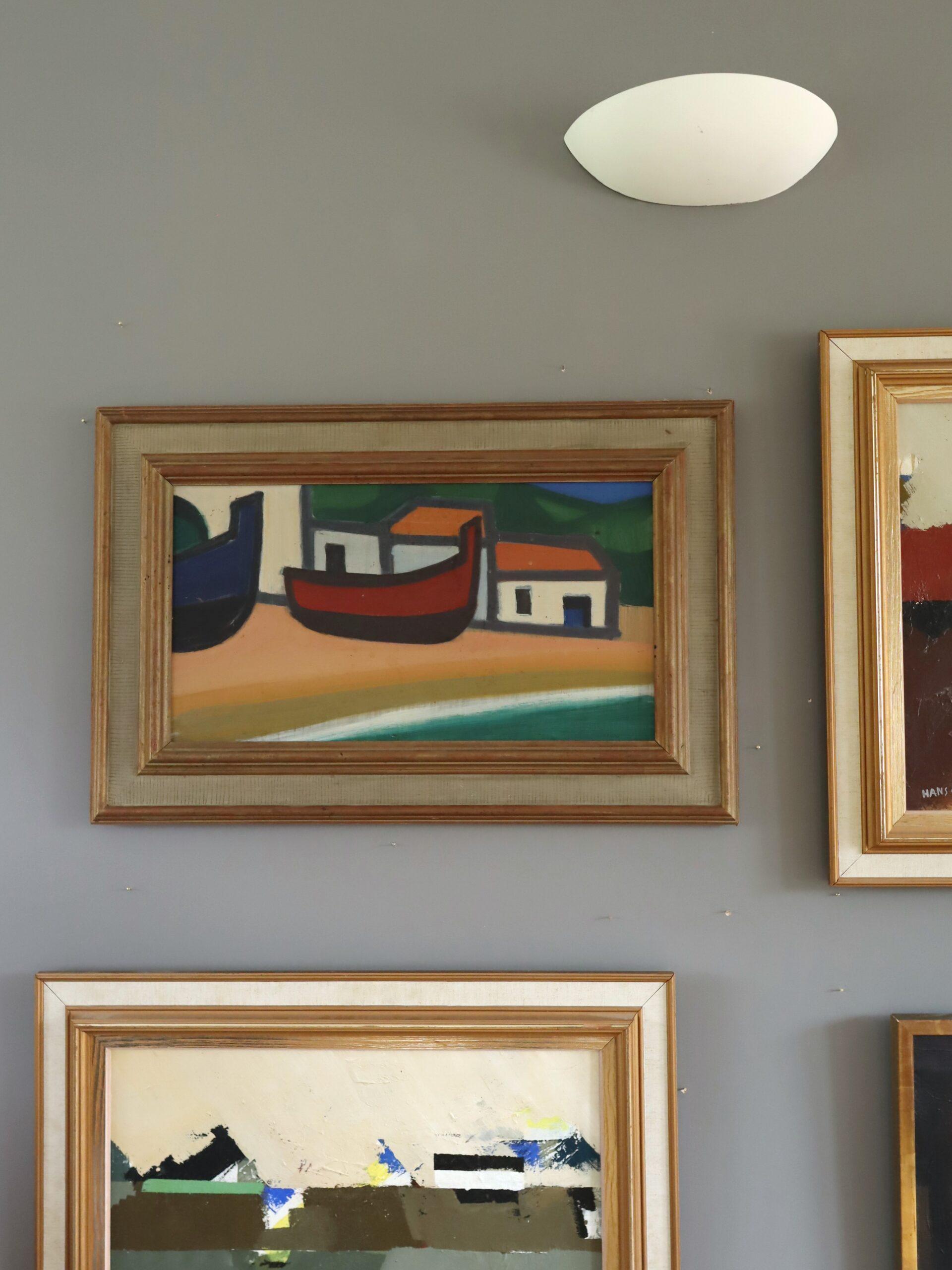 BOATS AT REST 
Size: 47.5 x 72.5 cm (including frame)
Oil on board

A striking mid-century modernist painting that captures the quiet charm of a coastal scene, executed in oil onto board.

Two boldly coloured boats – one in deep navy blue, the other