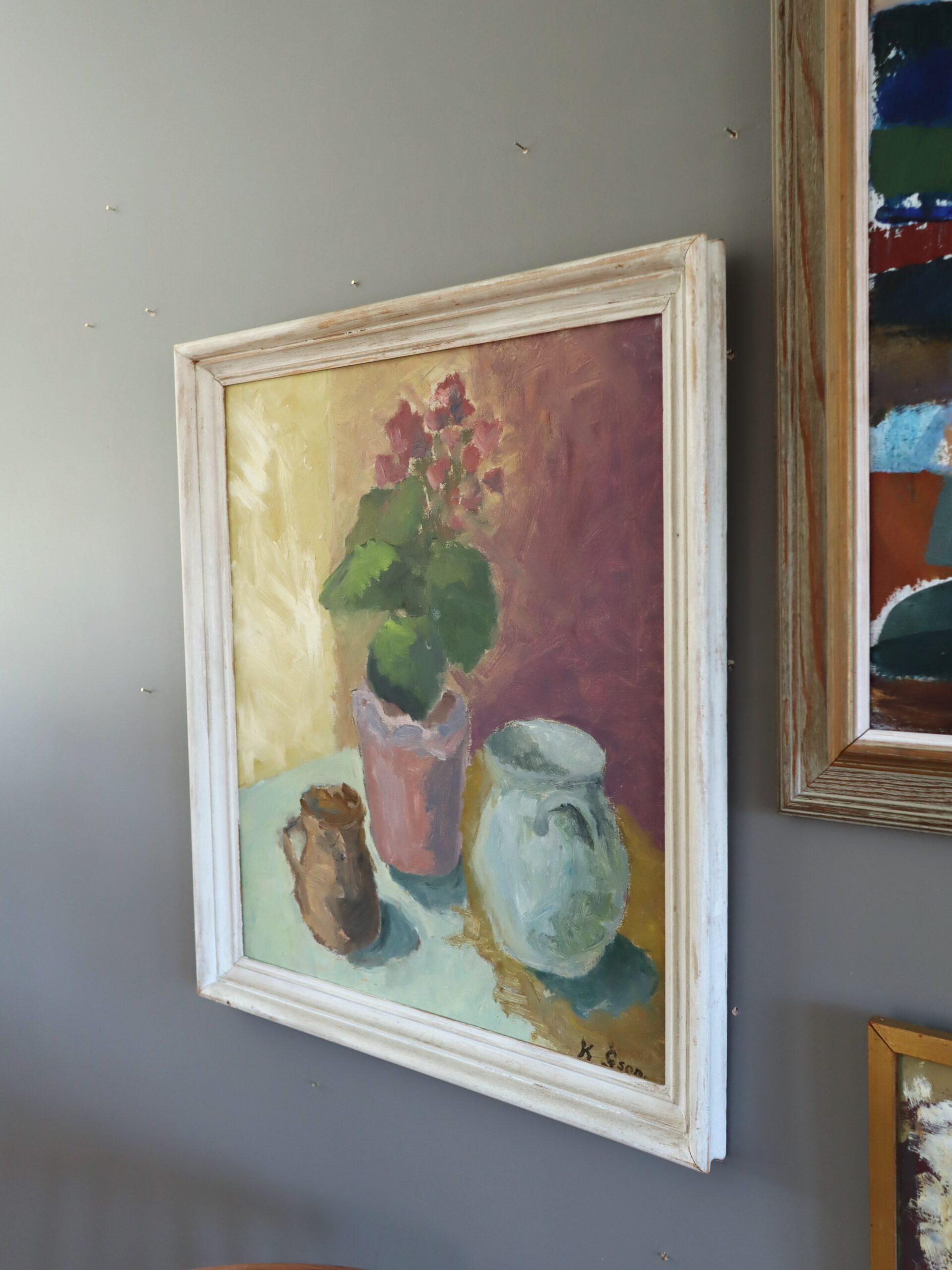 GÉRANIUMS ET CARAFES
Dimensions : 62 x 53 cm (cadre compris)
Huile sur carton

Une délicate et élégante composition de nature morte d'intérieur du milieu du siècle, peinte à l'huile sur carton.

Au cœur de la composition se trouve un géranium en