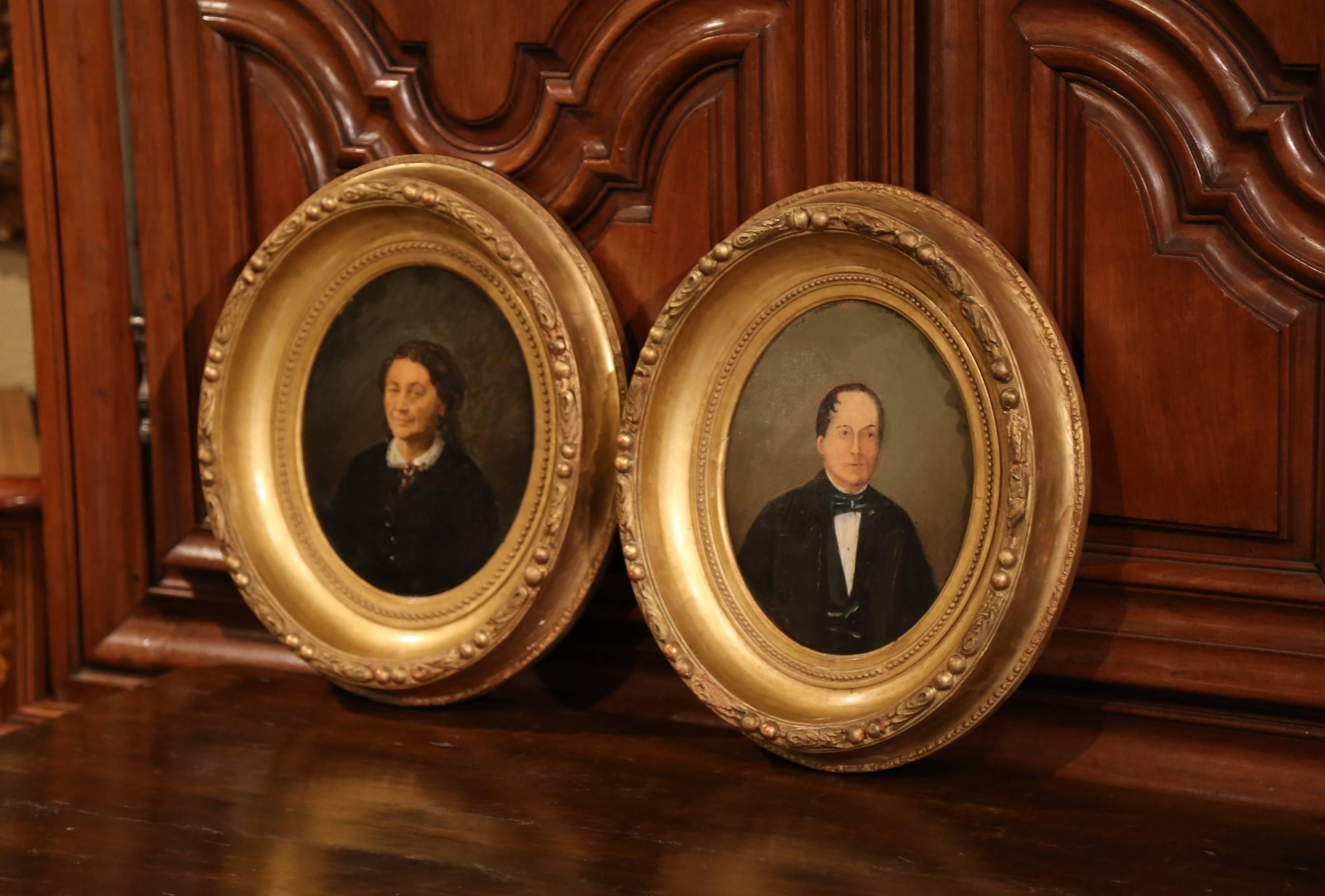This fine pair of antique portraits were painted in France in the 19th century. The oval paintings feature portraits of a man and a woman dressed in traditional clothing and painted on a board. They are both set inside their original carved oval
