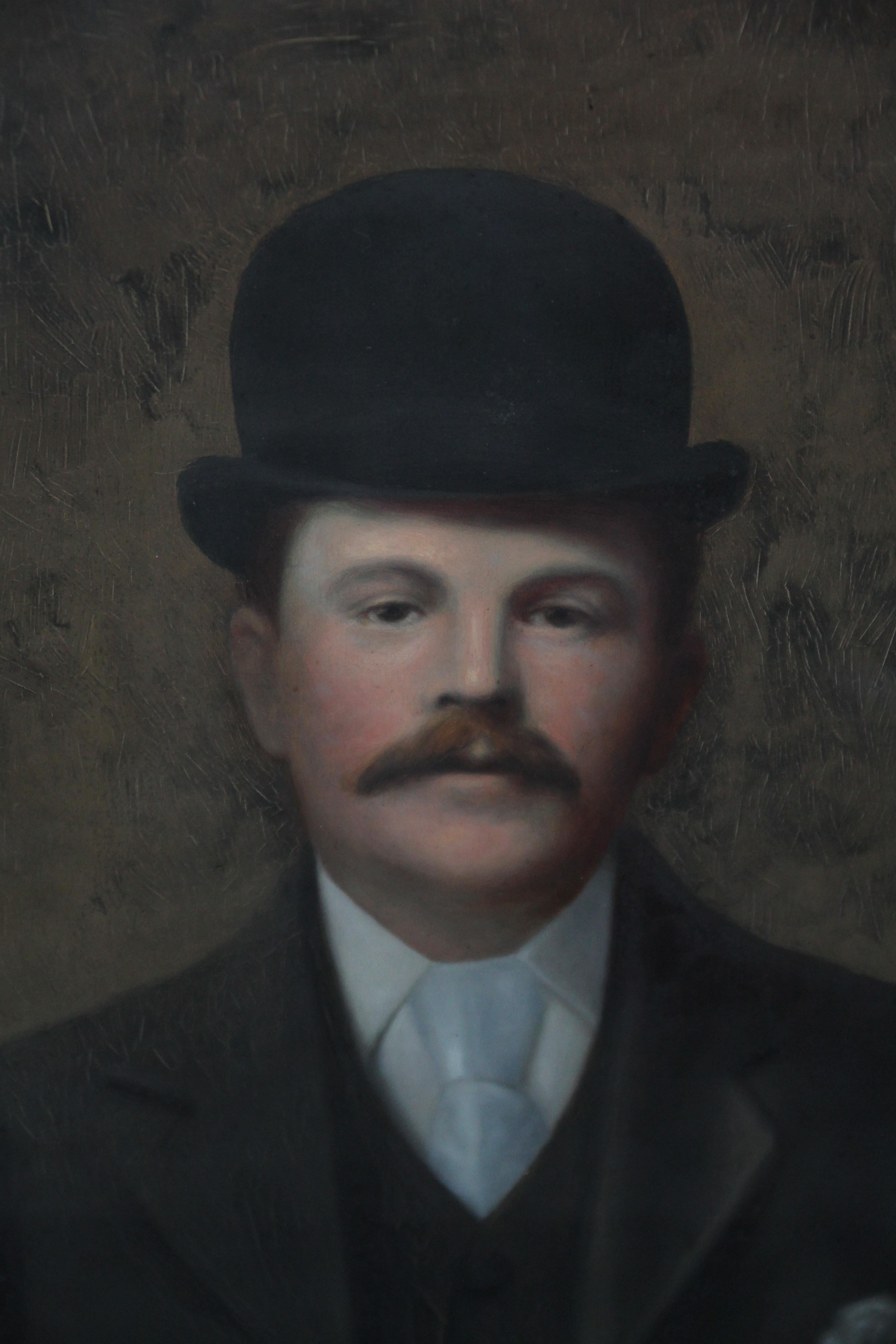 Dieses charmante britische Männerporträt in Öl zeigt einen Gentleman mit einem kultigen Bowlerhut. Gemalt um 1880 ist es ein wunderbares realistisches Weichzeichnerbild eines Mannes im Anzug mit breiter blassblauer Krawatte und Taschentuch in der