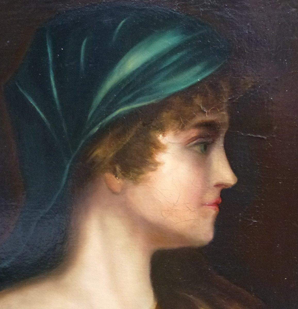 This late 19th-century oil on canvas exudes a sense of refined grace, characteristic of the art from this period. The portrayed woman, captured in profile, is a study in gentle luminosity against a deep, somber background. Her turquoise headscarf,