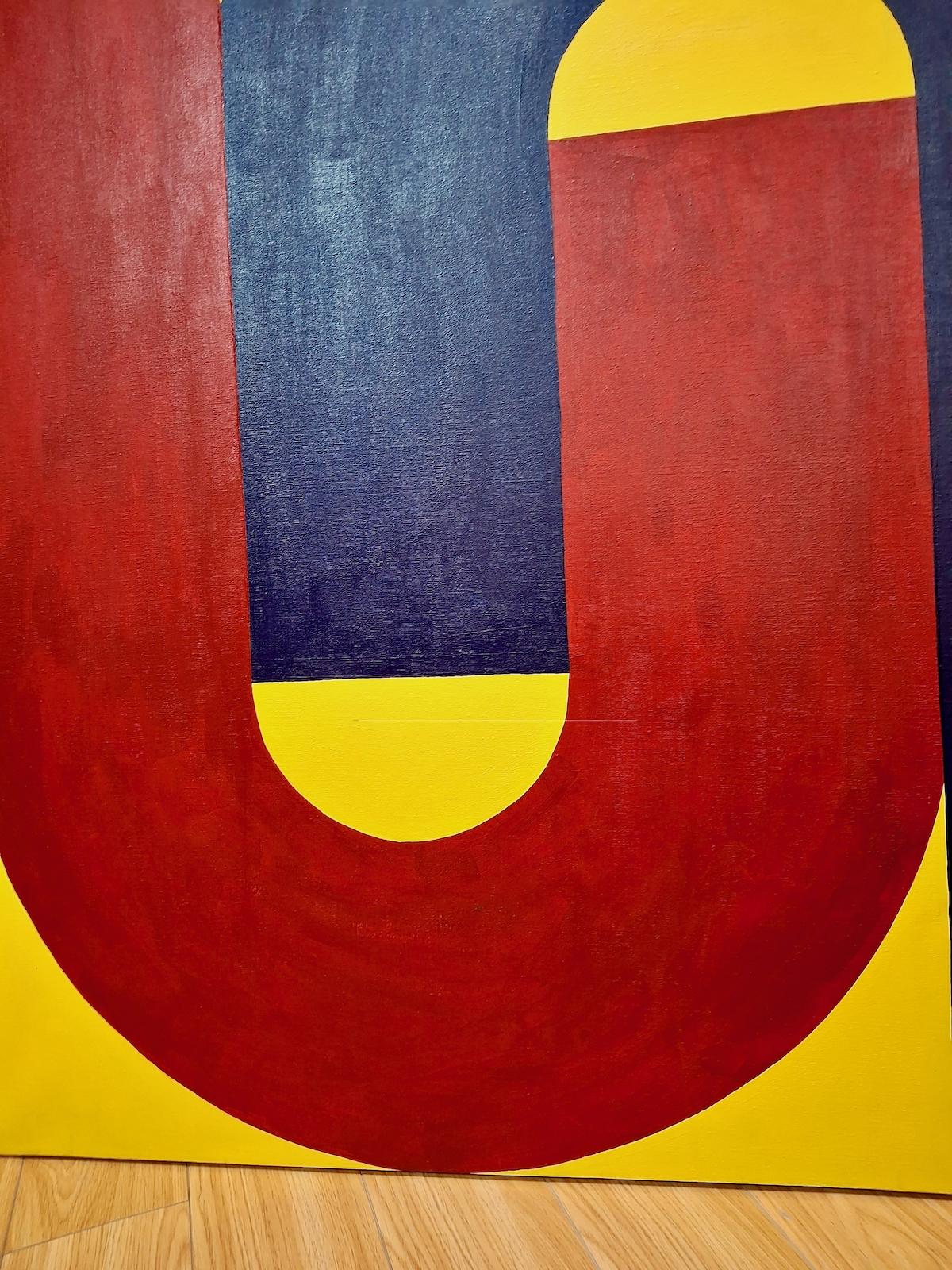 Locked in an embrace, two of the three primary colors set against a yellow background might represent the contentment of enduring intimacy, or the grip technology has on all of us, or even urban build out. But better still, whatever you can imagine.