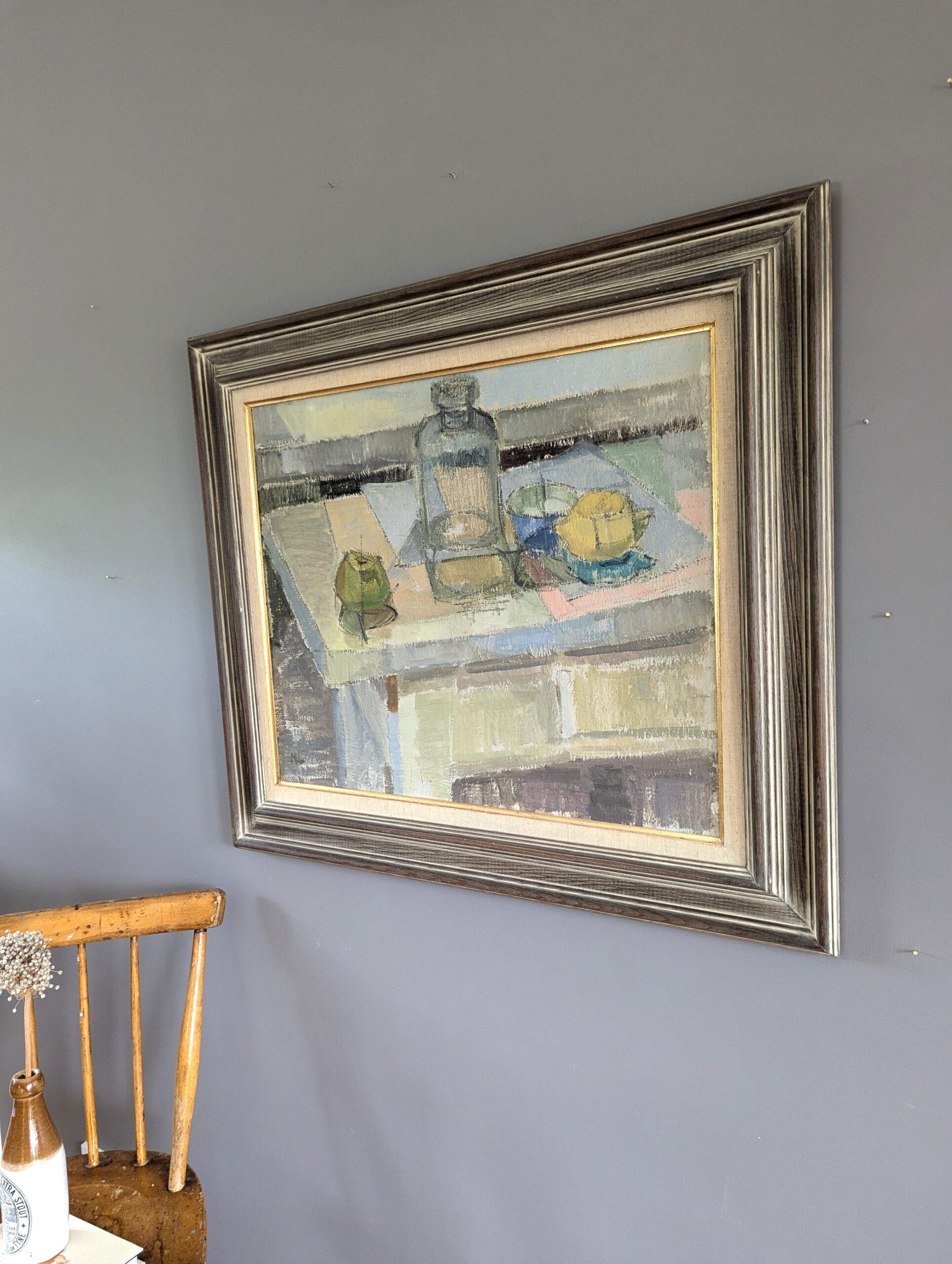 STILL LIFE WITH GLASS BOTTLE
Oil on Board
Size: 67.5 x 77.5 cm (including frame)

A brilliantly executed and gentle mid-century modernist style still life composition, executed in oil onto board.

A glass bottle, a green apple, a lemon, and a blue