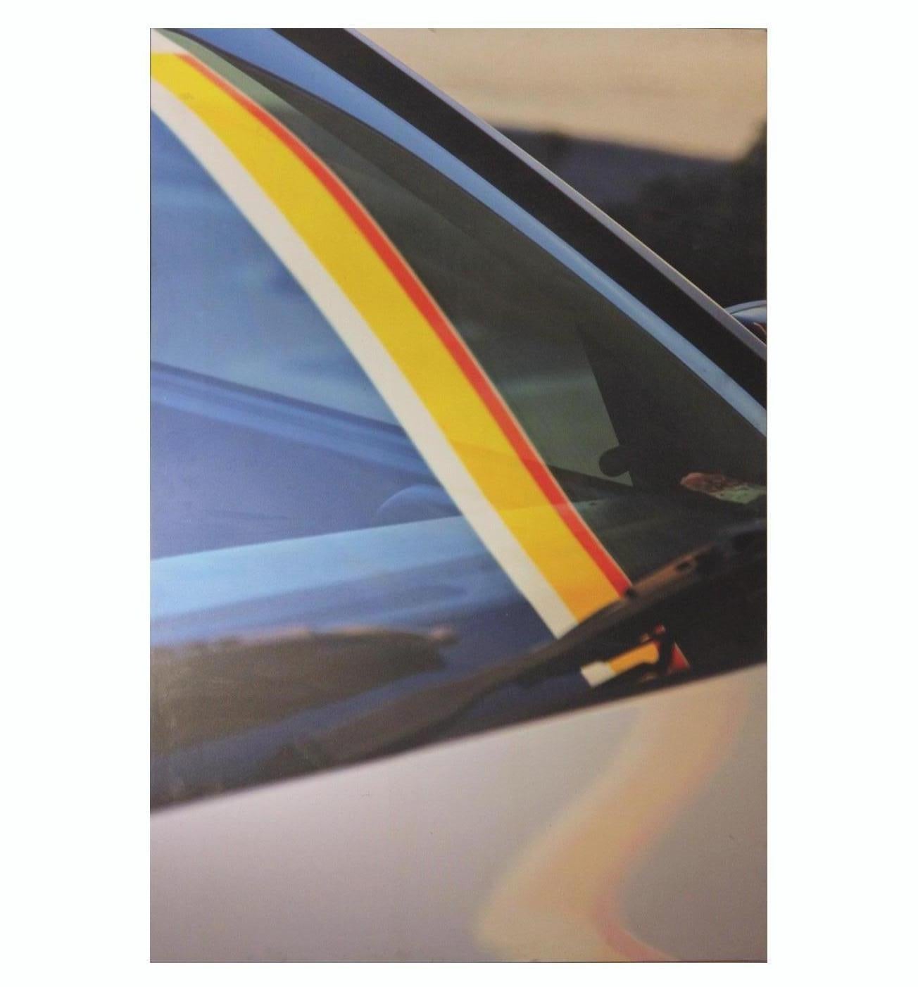 Close up photograph of a car with a reflection of what looks like a shell gas station awning. The photograph is printed on canvas and framed in a metal frame. 