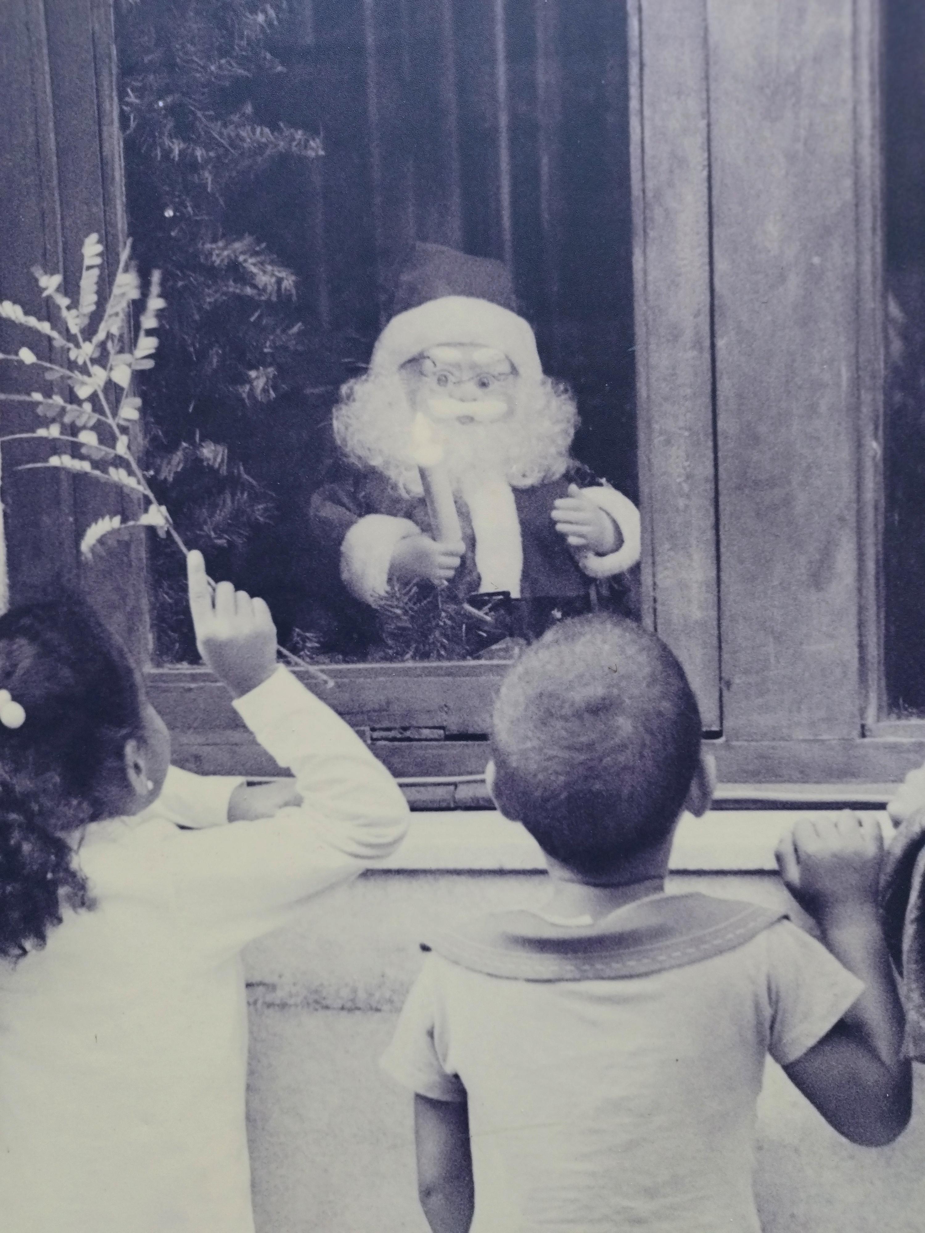 Rare photographie ancienne en noir et blanc sur papier sépia, elle représente trois enfants regardant le Père Noël à travers la fenêtre.
