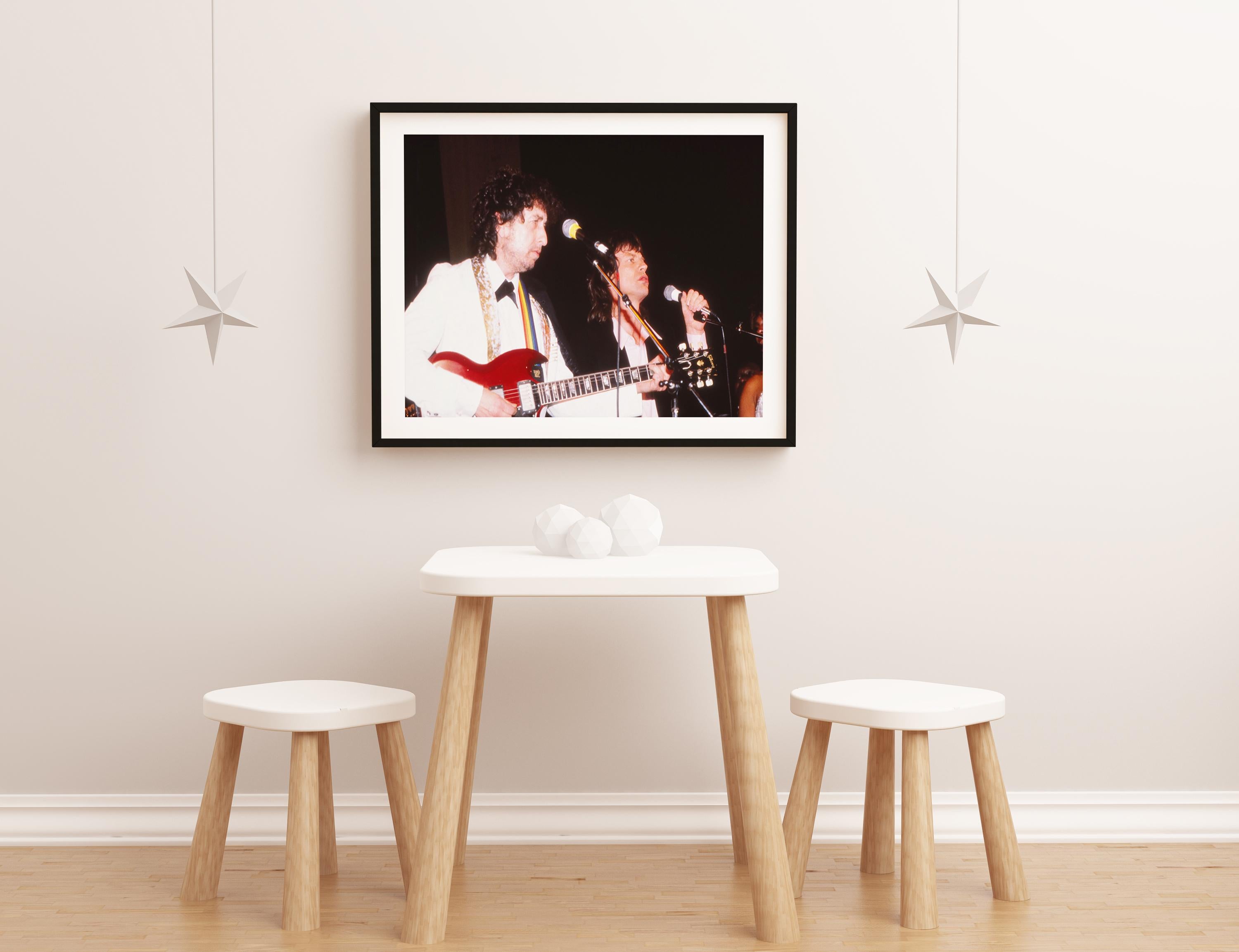 This color action shot features musicians Bob Dylan and Mick Jagger of the Rolling Stones performing together on stage. Bob Dylan is American singer-songwriter, author, and painter who has been an influential figure in popular music and culture for