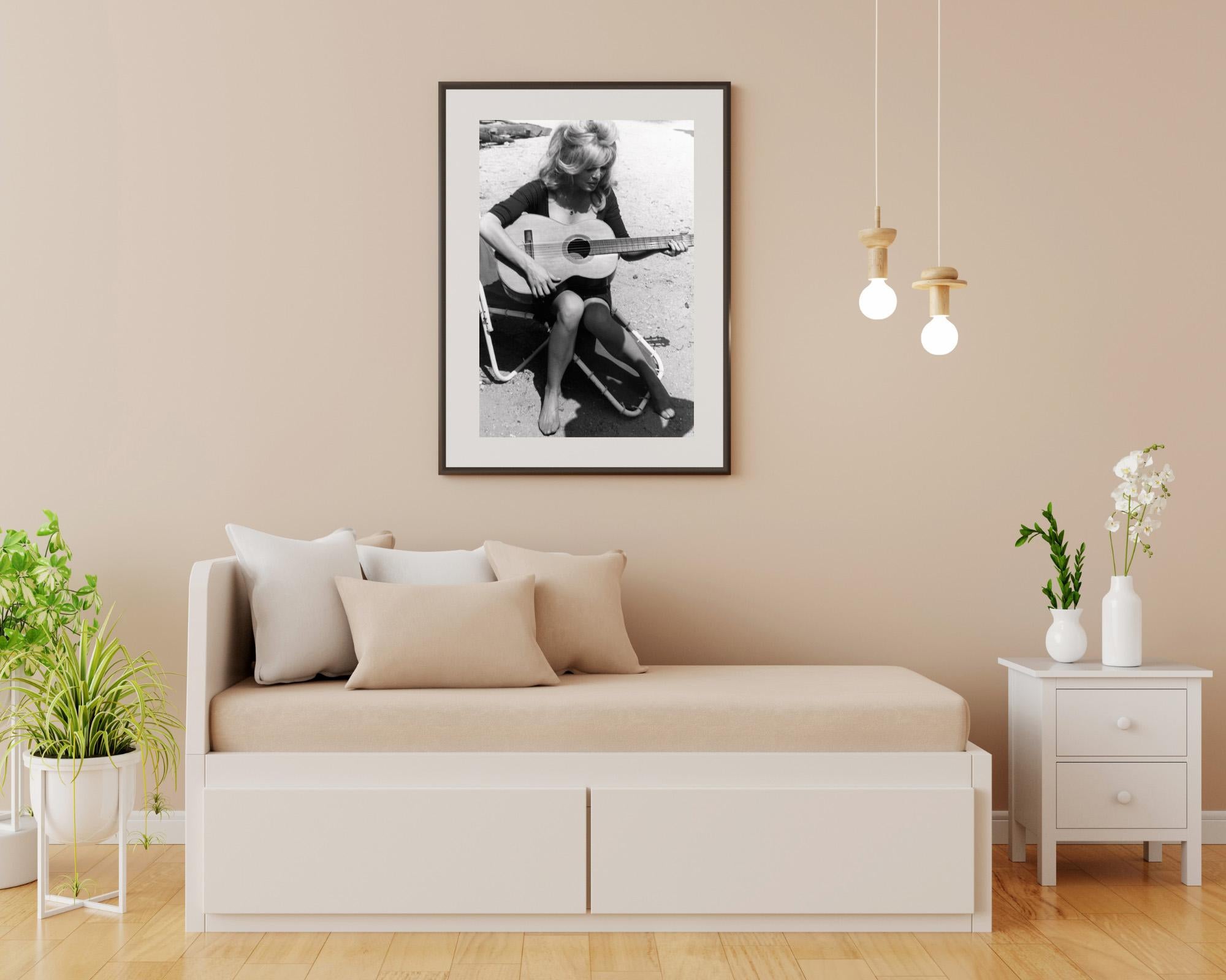 This black and white photo features Brigitte Bardot playing guitar on the beach.

Brigitte Bardot is a French actress and model who became an international sex symbol in the 1950s and 1960s. After retiring from acting, she devoted herself to